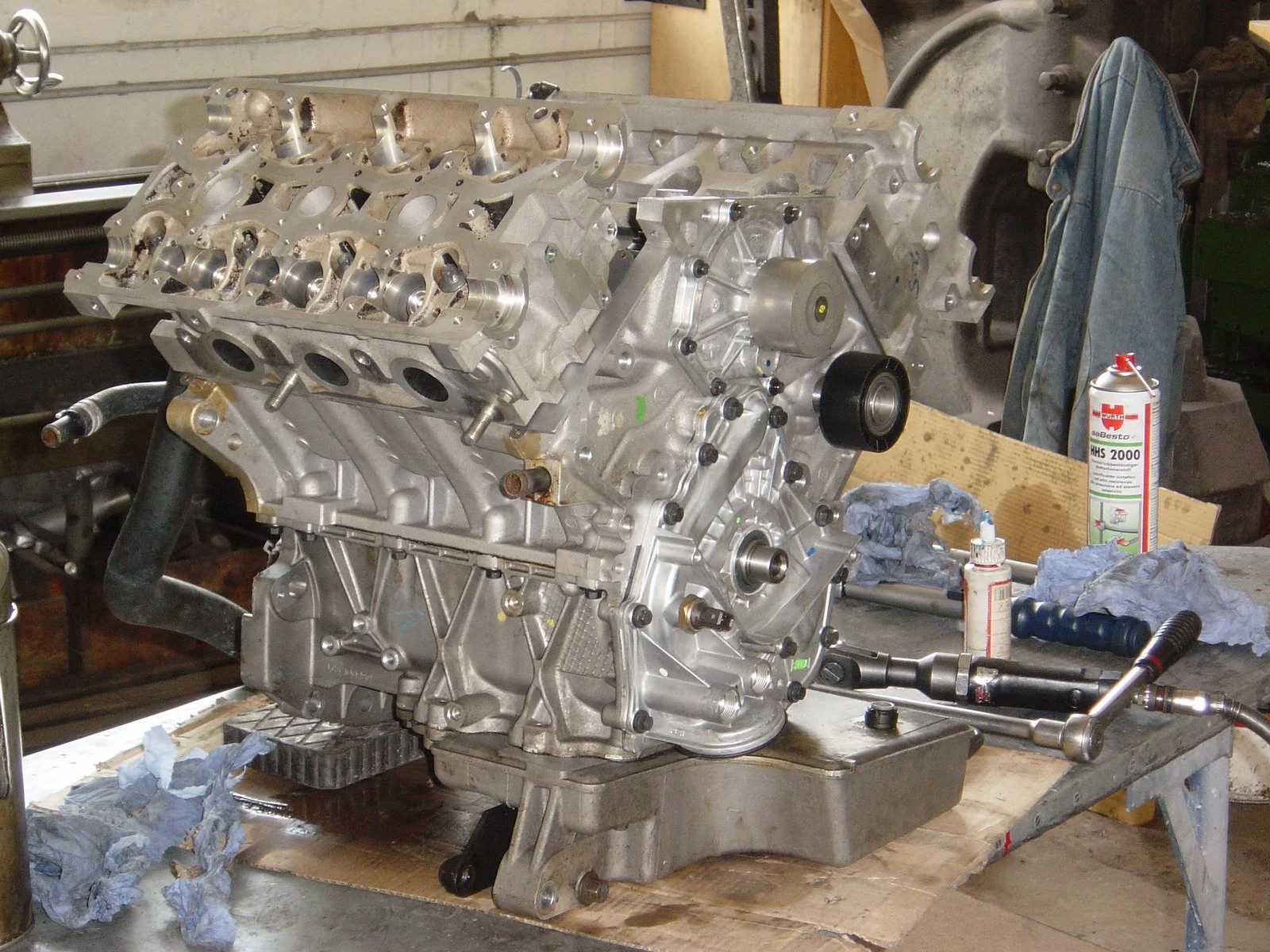 Brennraum eines Automotors auf einem Werkstatttisch, umgeben von Werkzeugen und Schmiermitteln.