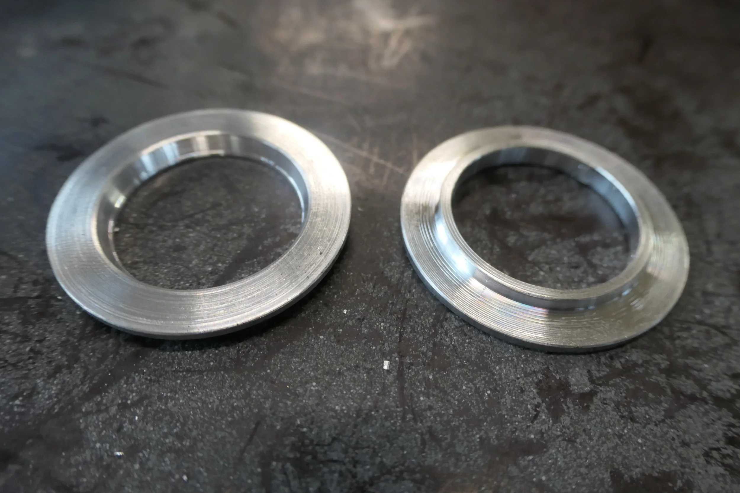 Zwei runde, silberne Metallringe mit gewölbtem Profil, die auf einer dunklen, rauen Oberfläche liegen.