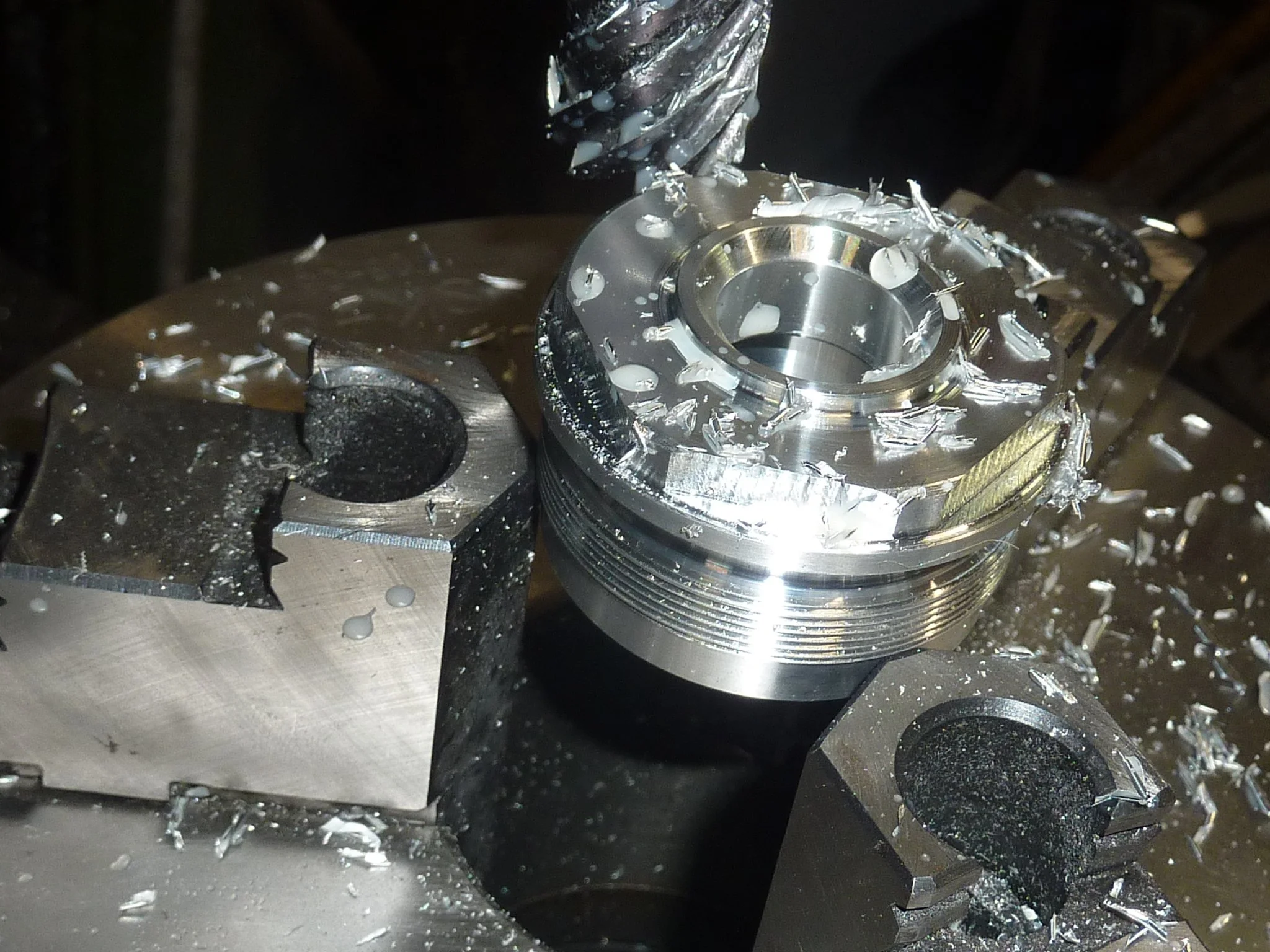 Ein metallischer Werkstück auf einer Maschine wird mit einem Bohrer bearbeitet, Metallspäne fliegen umher.