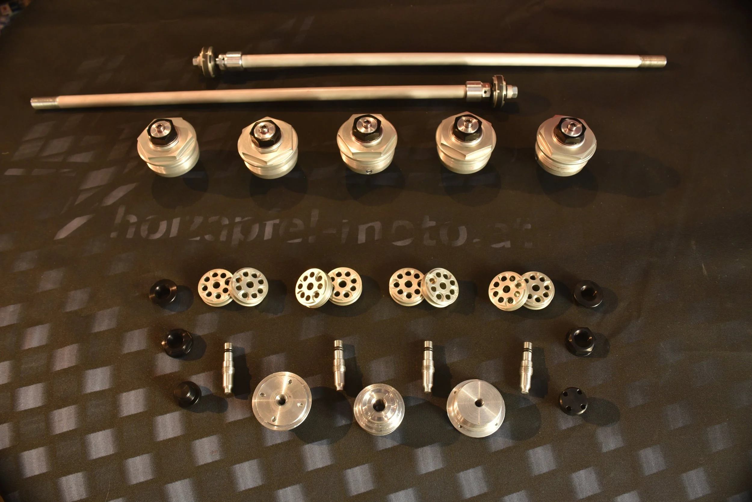 Mehrere Metallteile und Schrauben für den Zusammenbau eines Fahrzeugs oder einer Maschine, auf einem dunklen Untergrund