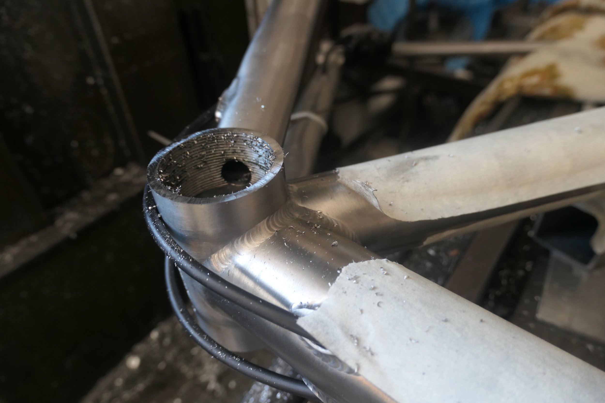 Nahaufnahme eines Metallrahmens mit geschweißten Verbindungen, vermutlich Teil eines Fahrrads oder eines Rahmens, in einer Werkstatt