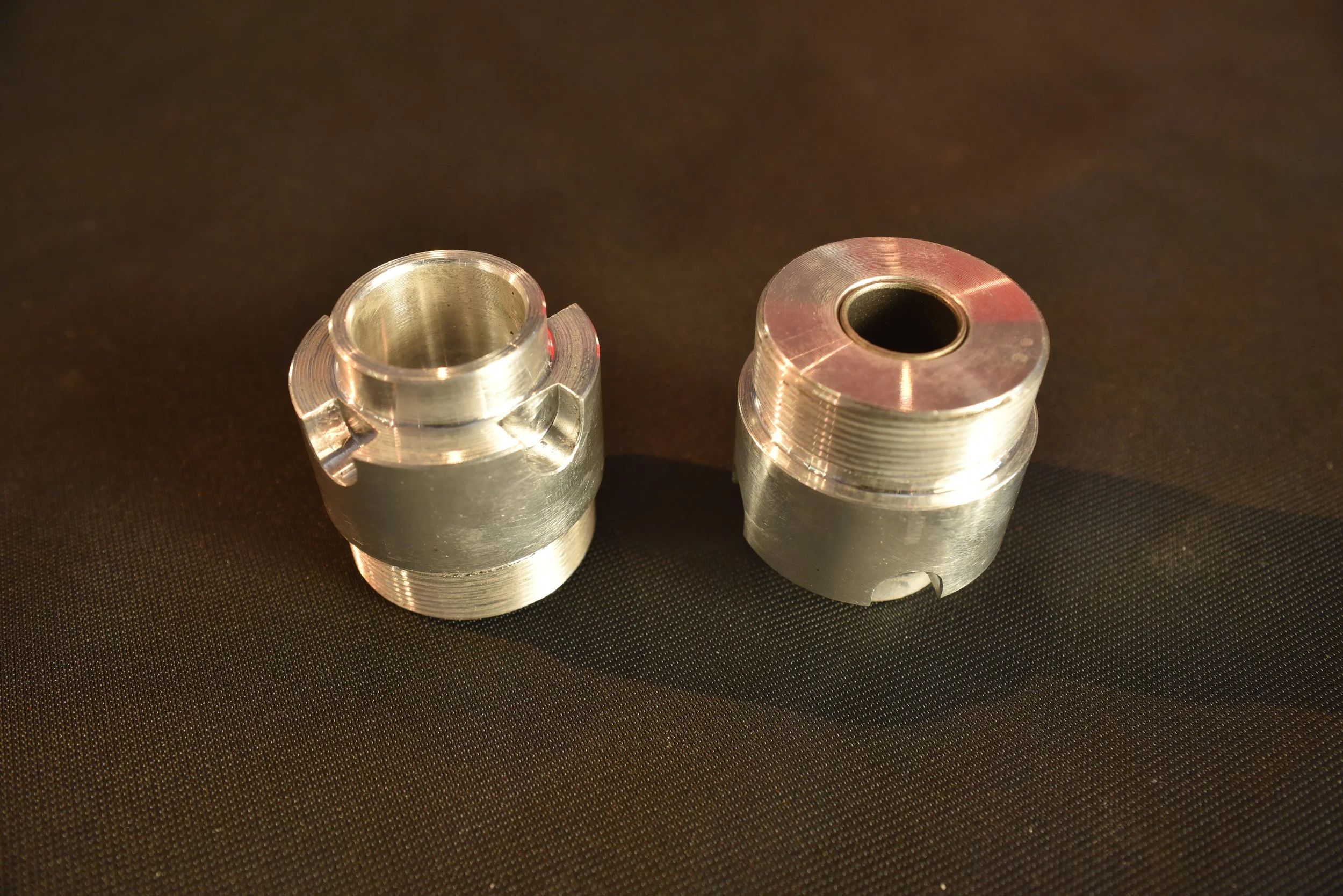 Zwei silberne Metallteile mit Gewinde und Kerben auf schwarzem Hintergrund.