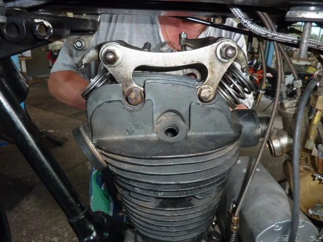 Nahaufnahme eines Motorradmotors, der bei der Reparatur oder Wartung ist, mit sichtbaren Zylindern, Ventilabdeckungen und Verbindungselementen.