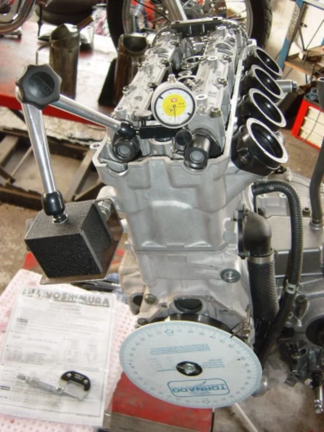 Ein Auto- oder Motorradmotor in einem Werkstattumfeld, mit Messinstrumenten und Werkzeugen um ihn herum.