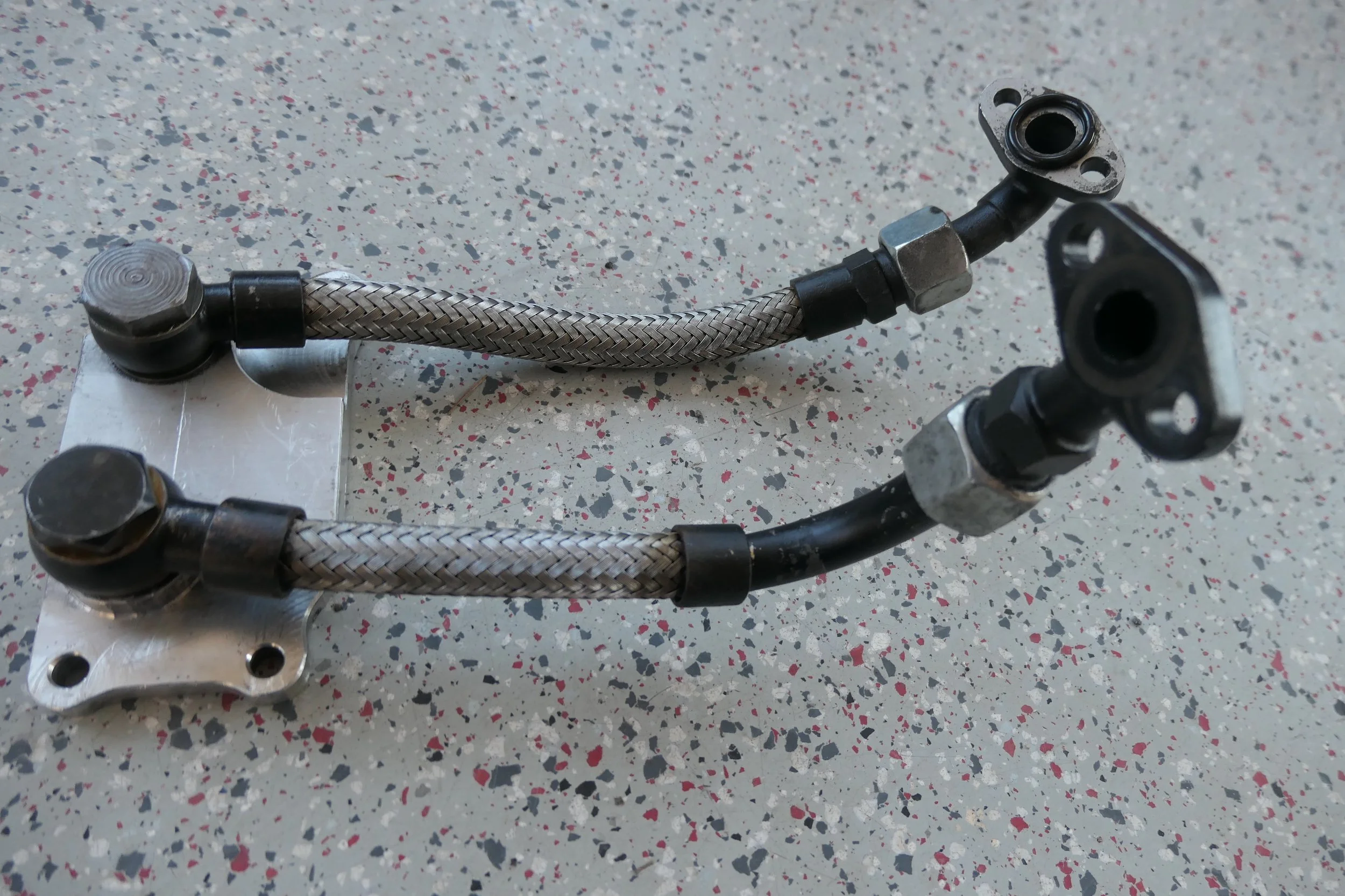 Zwei Kraftstoffleitungen mit Metallfassungen und flexiblen Silikonschläuchen auf einer Arbeitsplatte.