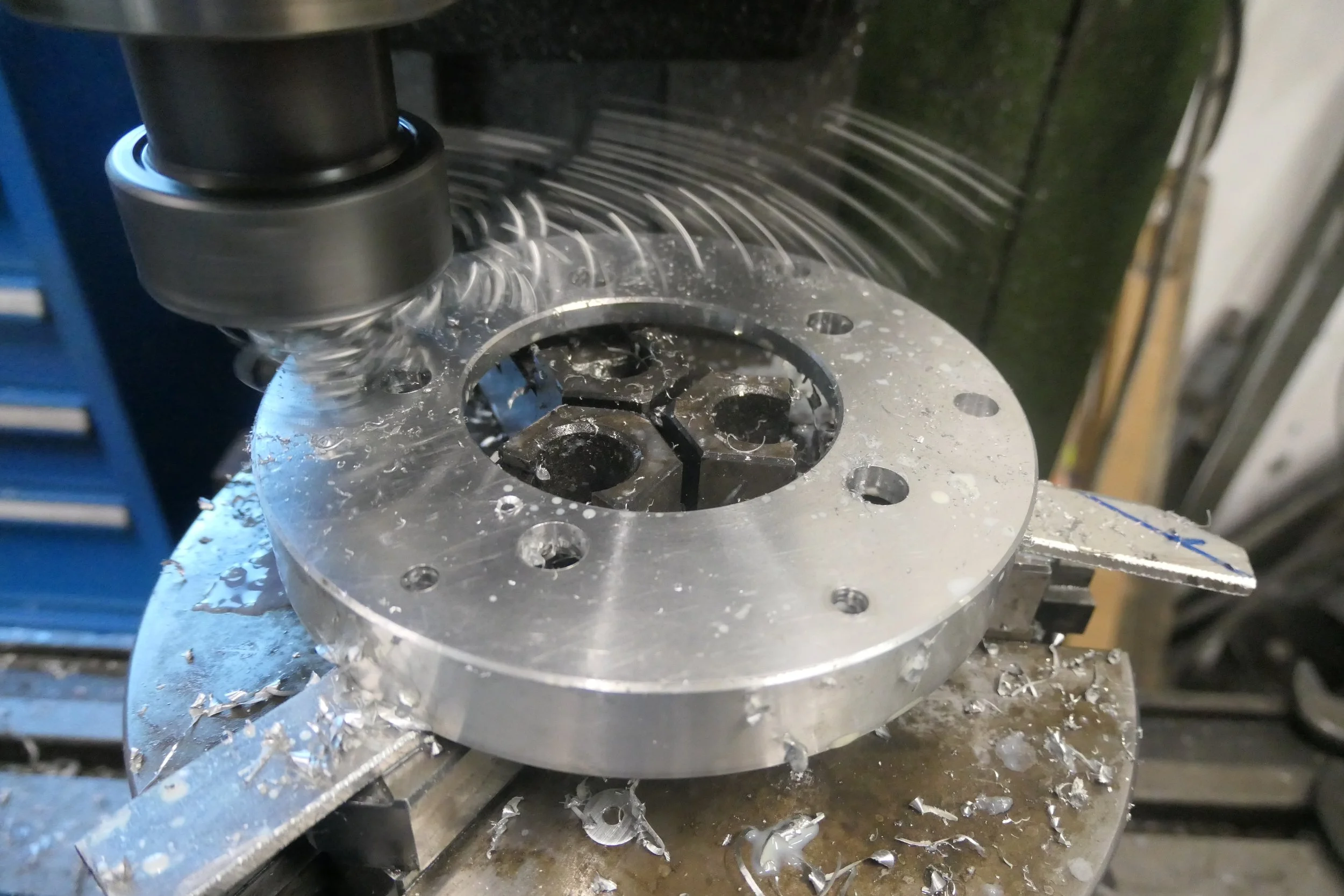 Metallbearbeitung mit Fräsmaschine, die eine runde Metallplatte bearbeitet. Späne und Metallreste liegen auf dem Tisch