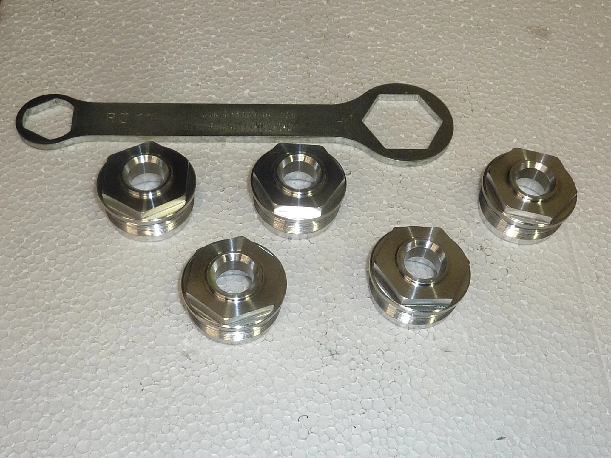 Sechs metallene Radmuttern und ein Ringschlüssel auf weißem Polystyrol.