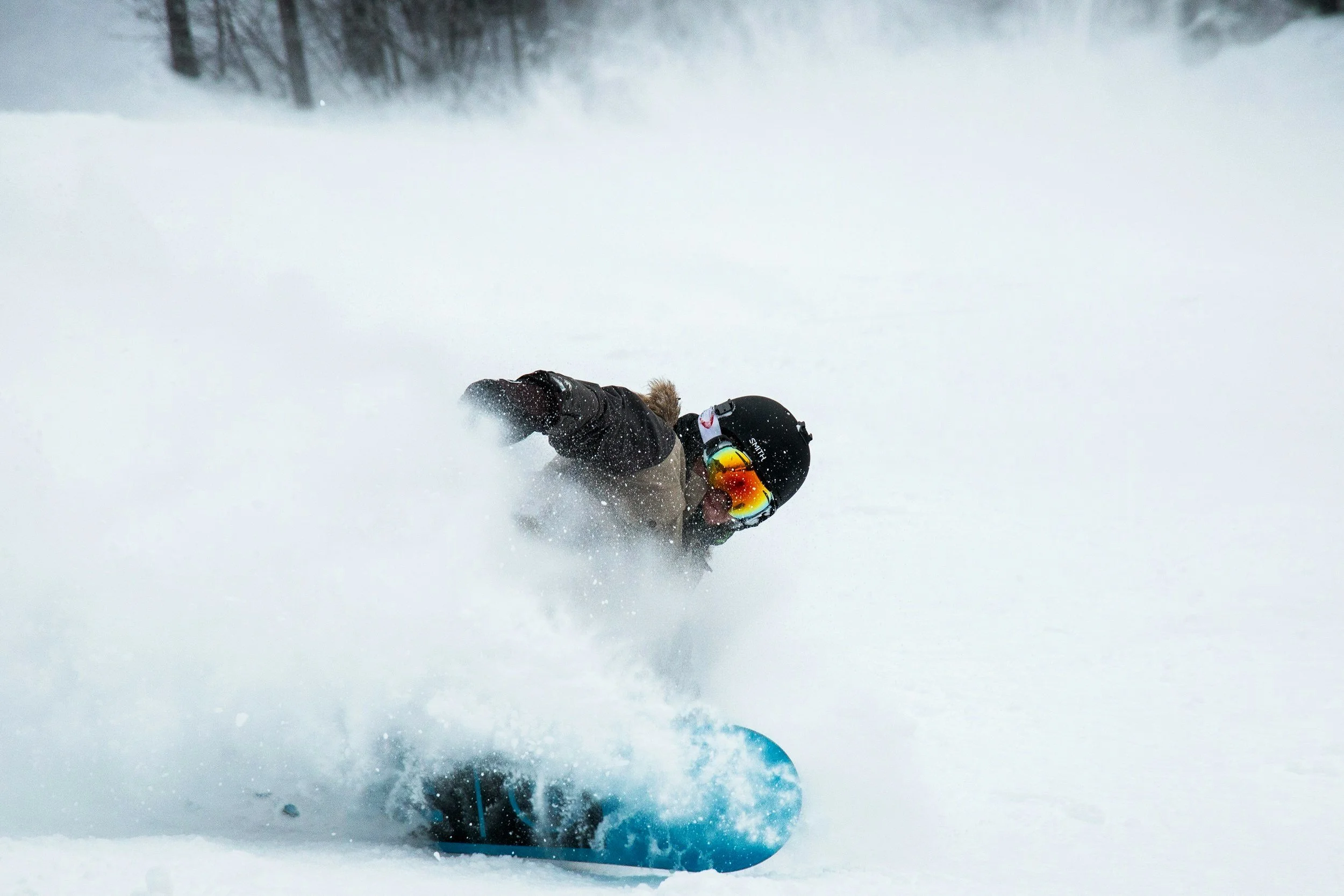 A person snowboarding down a snowy slope, wearing a black helmet, goggles, a winter jacket, and gloves, surrounded by snow.