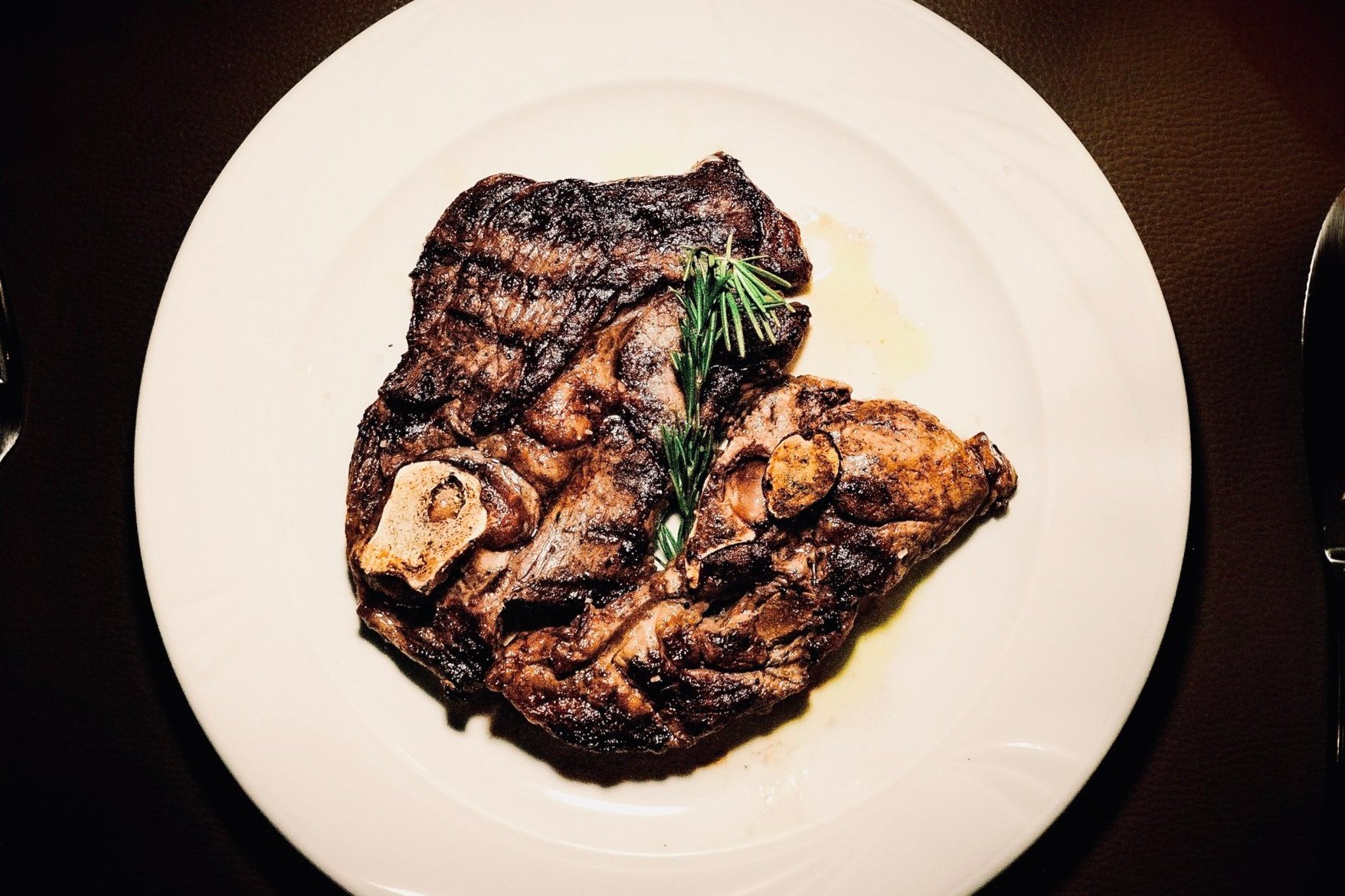 Un piatto di carne di manzo con ossa, cotta e servita con un rametto di rosmarino sopra, su un piatto bianco