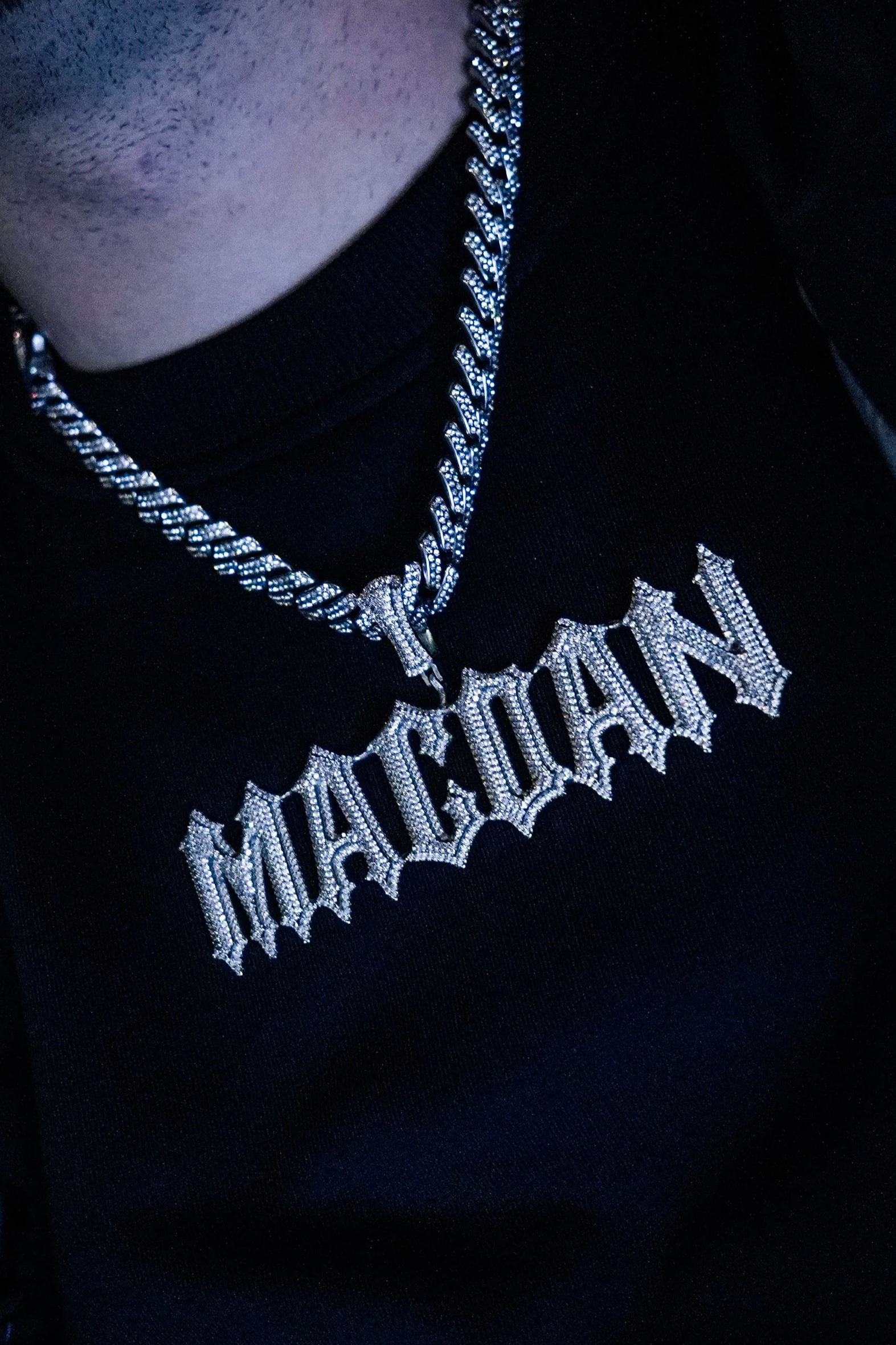 Collana e ciondolo con la scritta "MACHIAVELLA" in diamanti, indossati da una persona con maglietta nera.