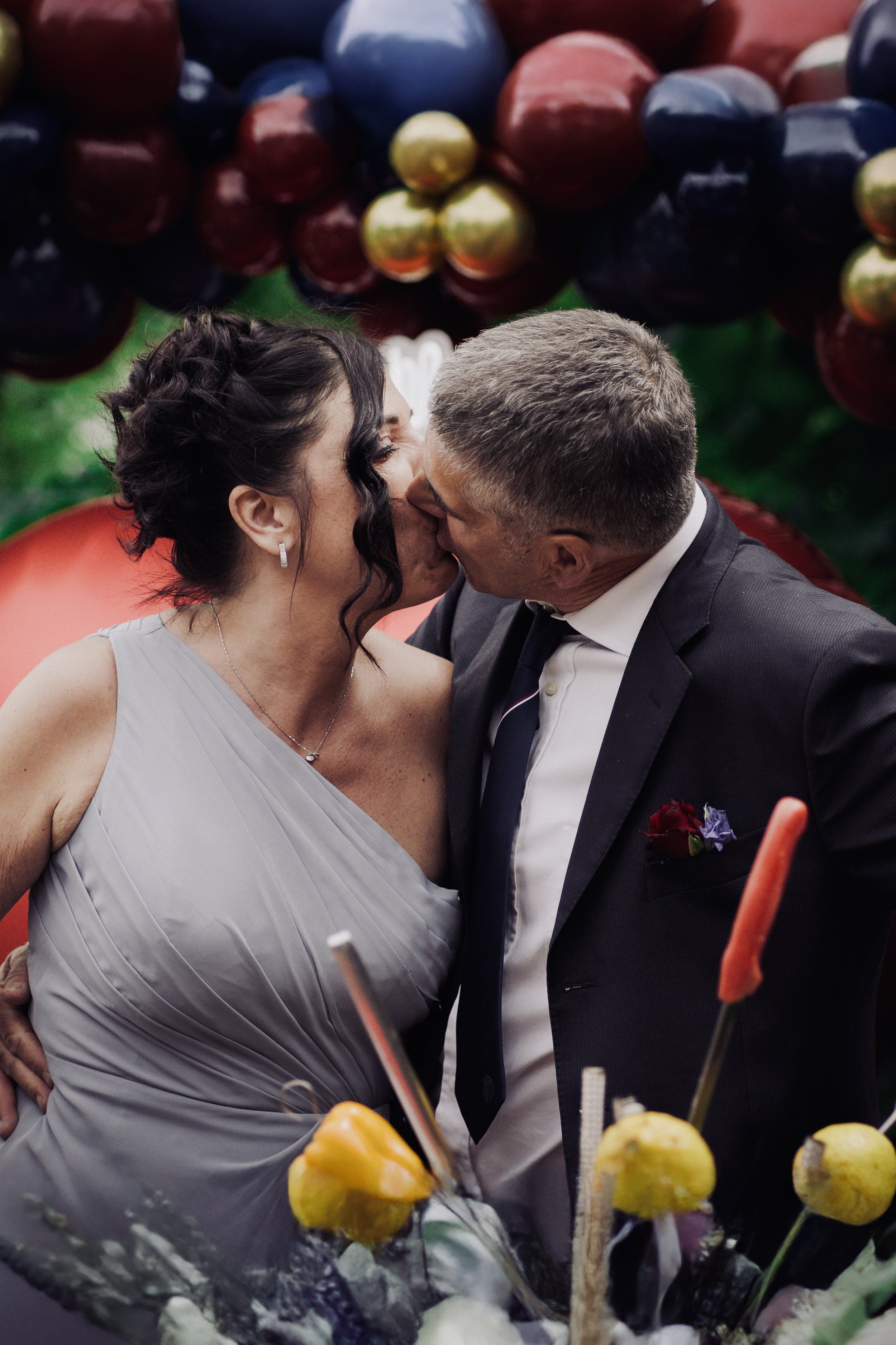 Una coppia si bacia in festa, circondata da decorazioni di frutta, come uva e mele, durante un matrimonio o un evento simile.