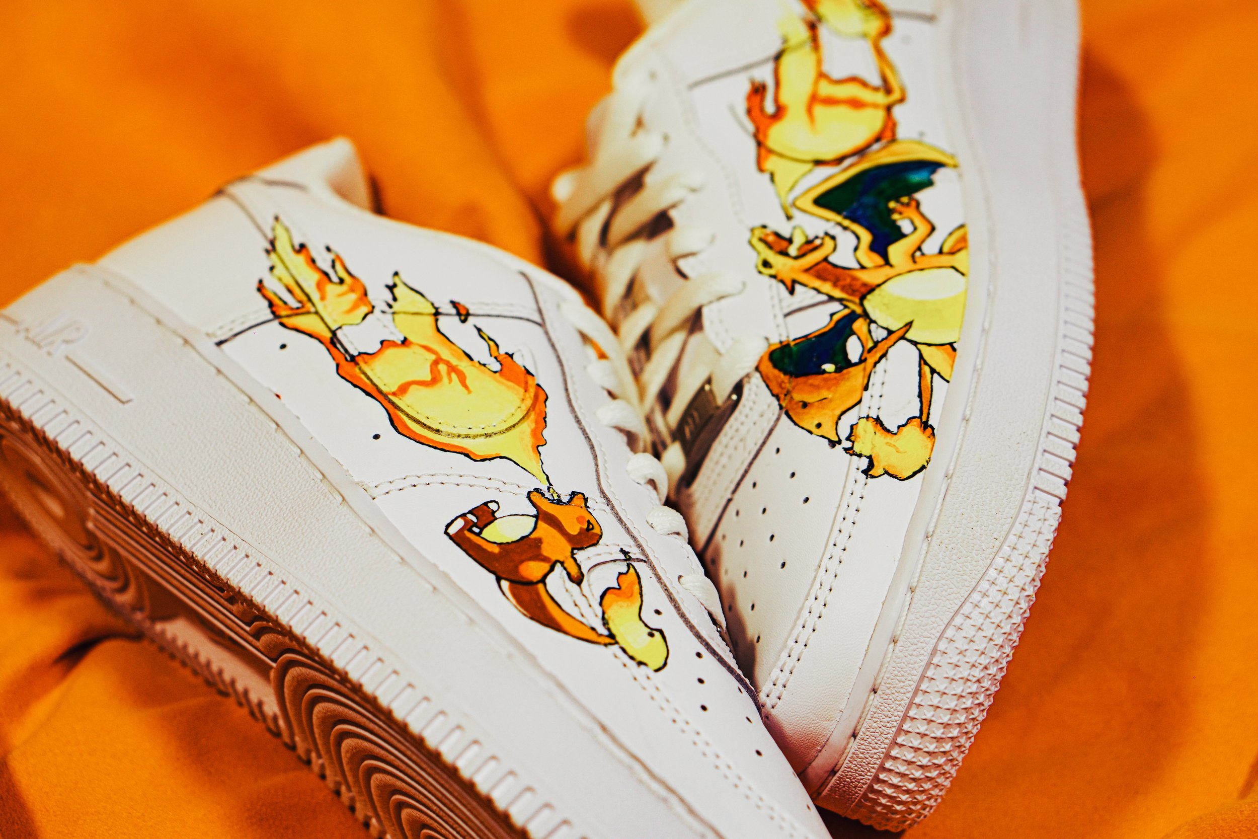 Scarpe da ginnastica bianche con disegni colorati di figure stilizzate e fantasiose, poggiate su un fondo arancione.