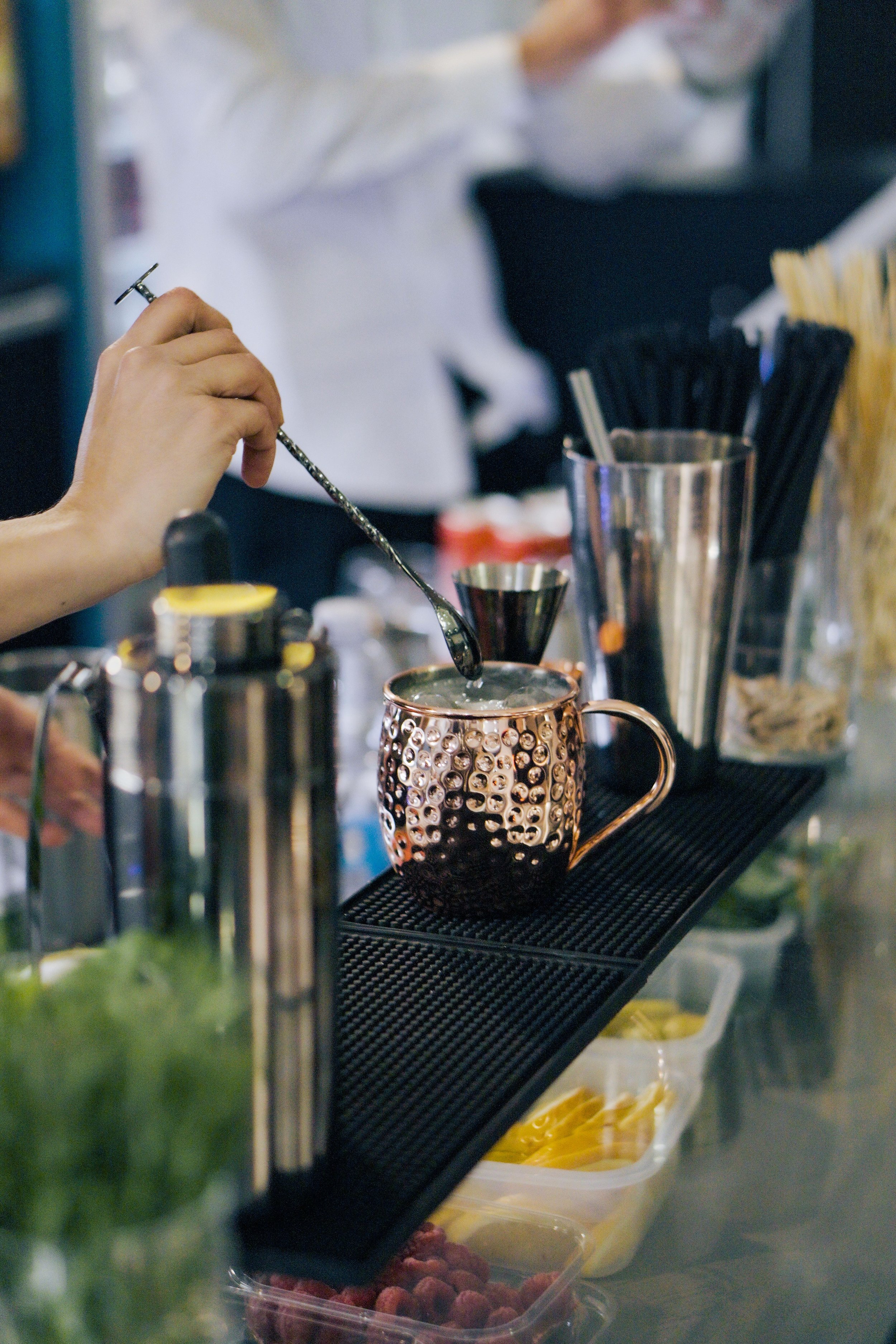 Una mano sta versando uno sciroppo caldo in una tazza di ceramica decorata con bolle durante la preparazione di una bevanda, probabilmente un caffè o tè, al bancone di un bar.
