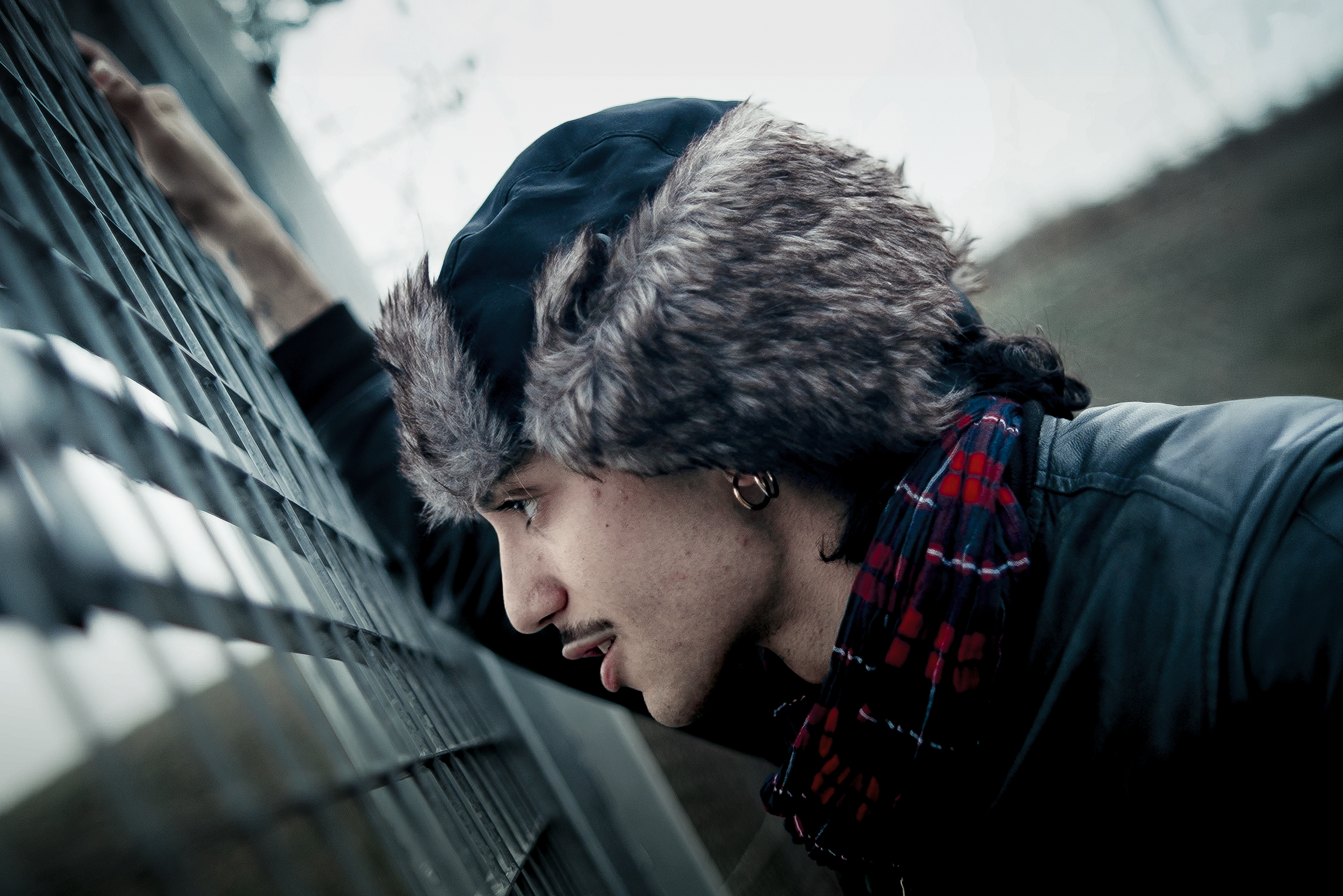 Uomo con cappello di pelliccia e orecchino che guarda attraverso una recinzione di metallo