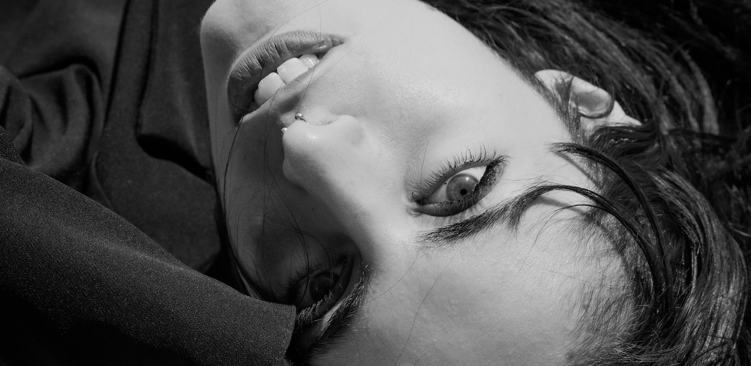 Ragazza con capelli scuri, occhi chiusi o semi-chiusi, sorridente, quella sul letto o su una superficie morbida, vestita di nero, in bianco e nero