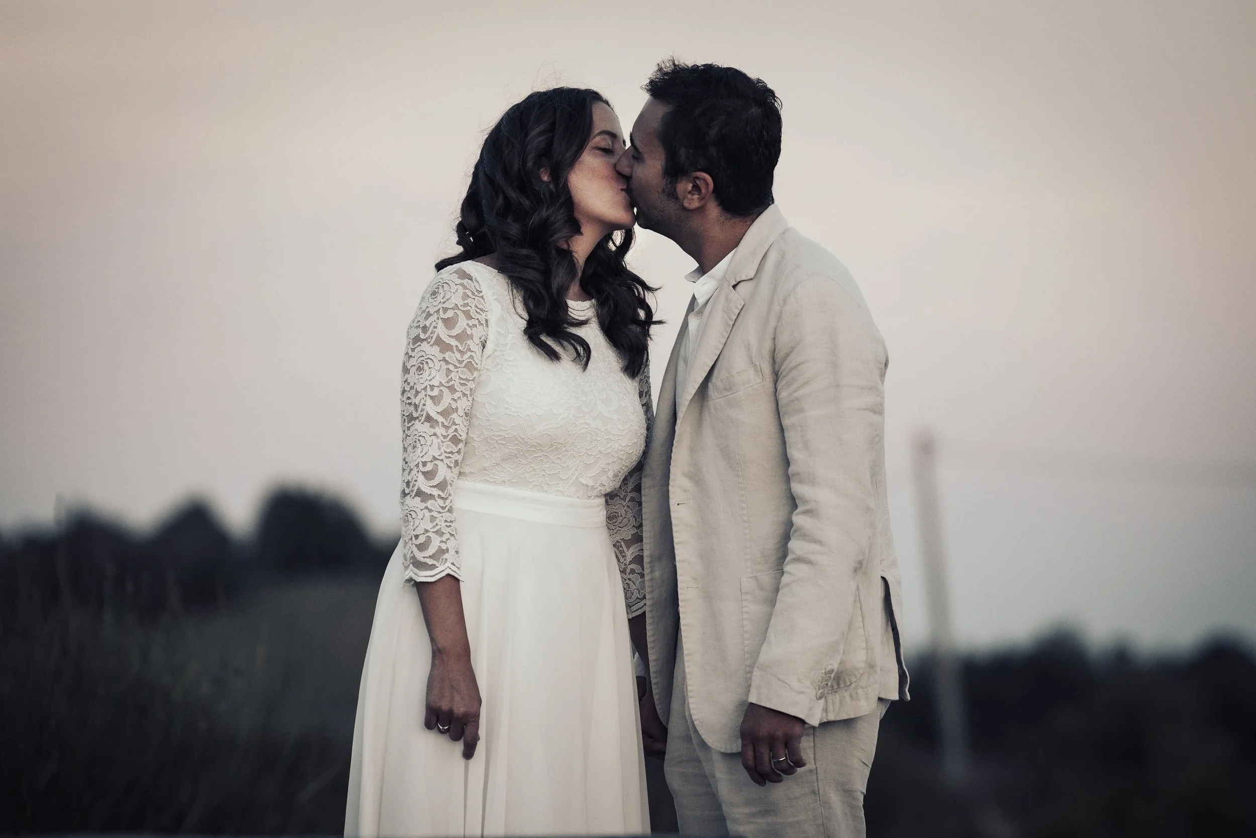 Una coppia si bacia appassionatamente all'aperto, indossando abiti eleganti, con uno sfondo di cielo al tramonto.