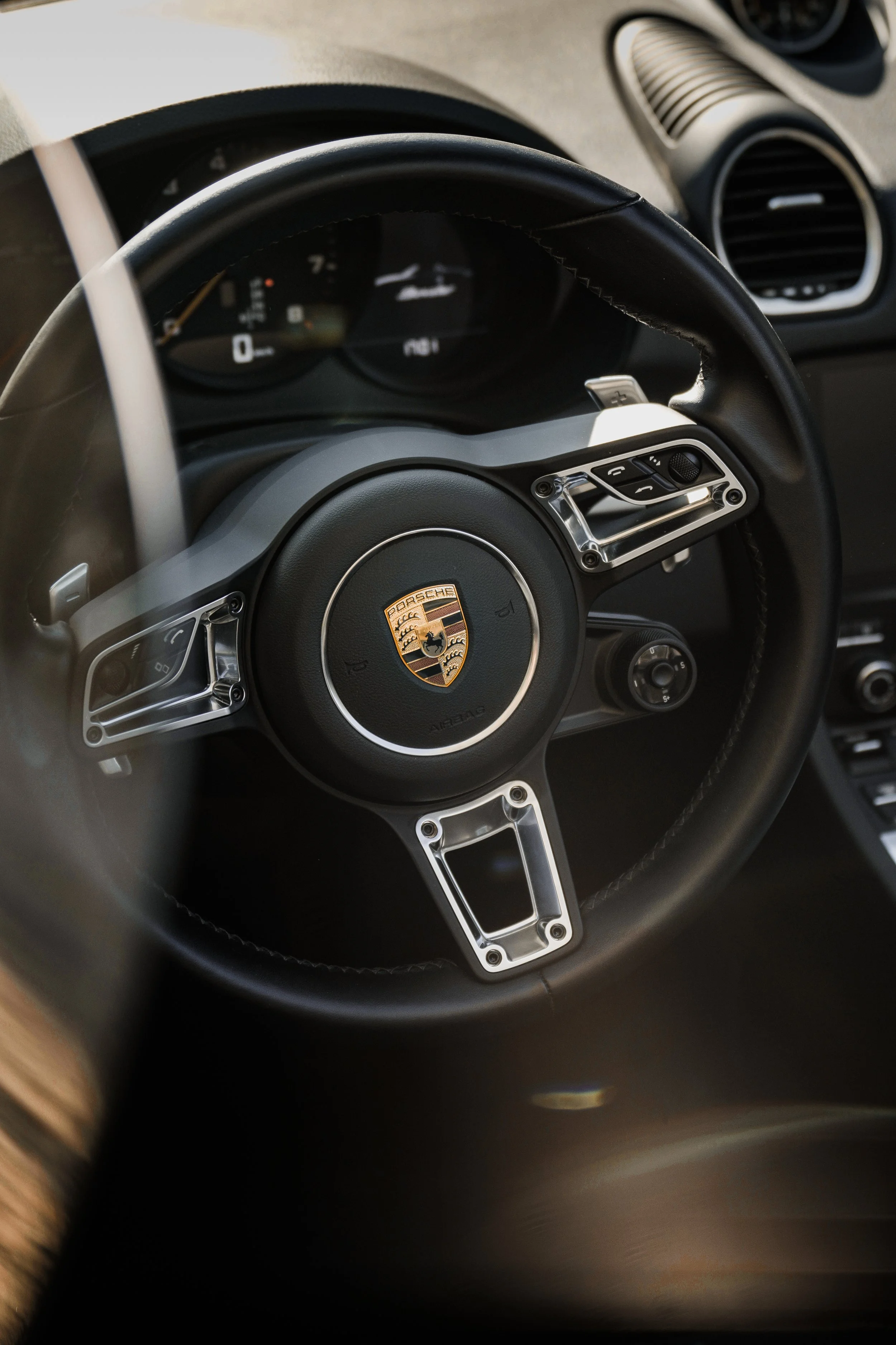 Volante di una Porsche con logo centrale, comandi sui lati e parte del cruscotto visibile.