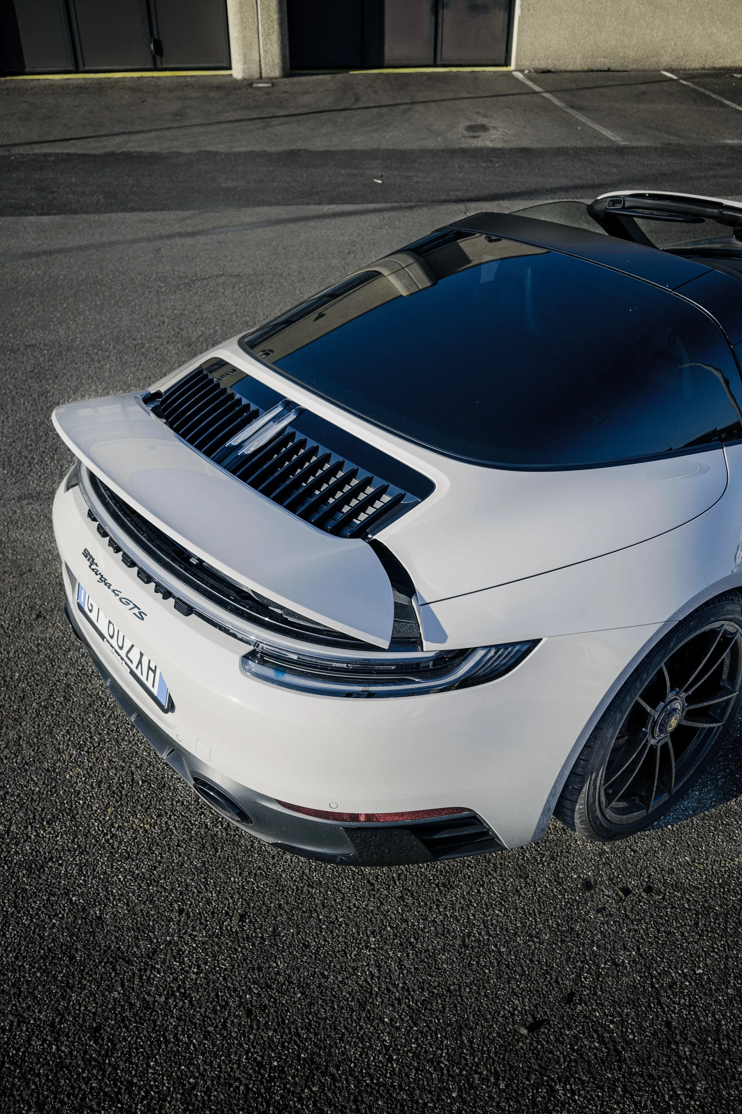 Auto sportiva Porsche 911 Targa GTS bianca parcheggiata su strada asfaltata con un soffitto in vetro oscurato.