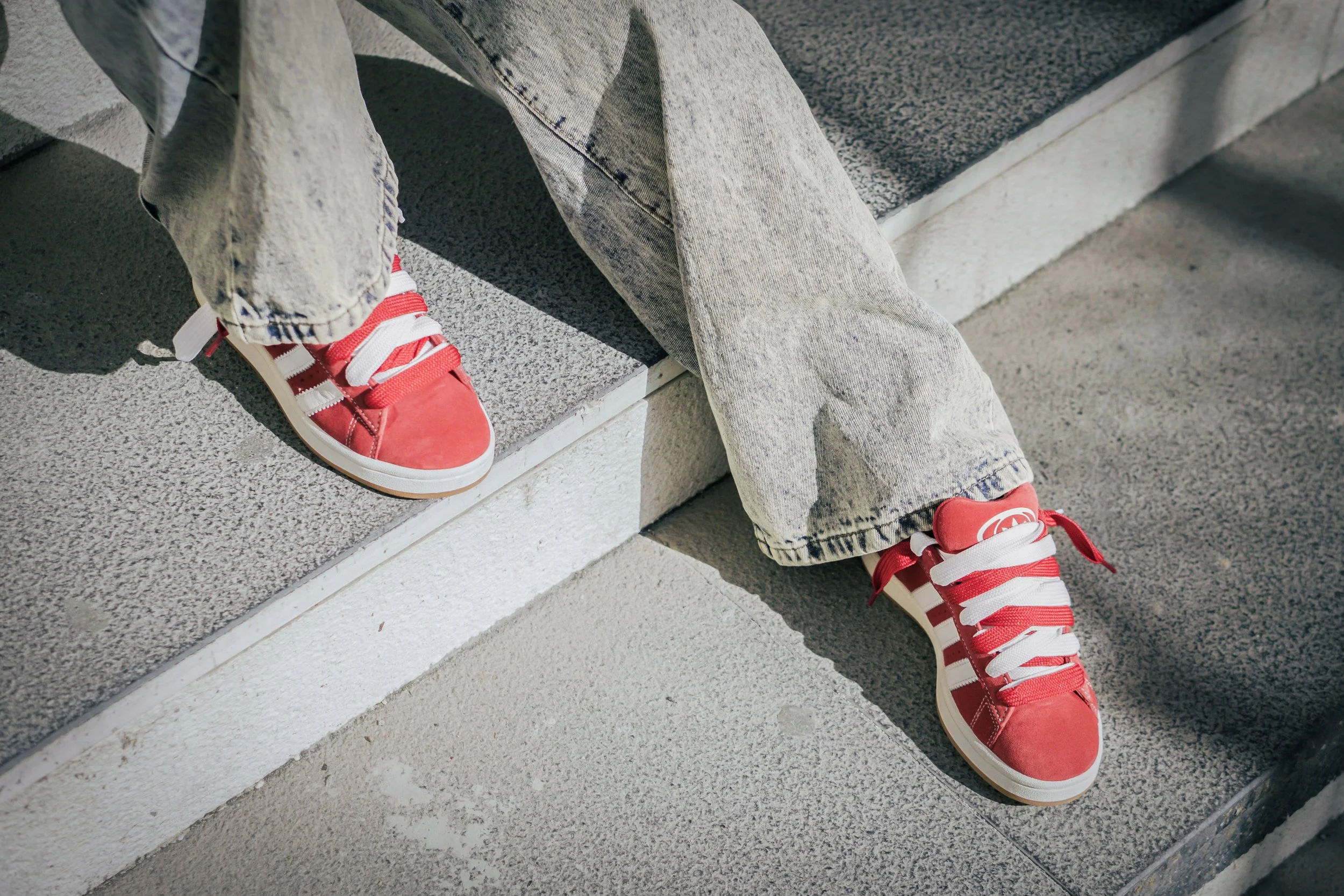 Persona seduta sulle scale, indossa scarpe rosse e pantaloni di jeans beige.