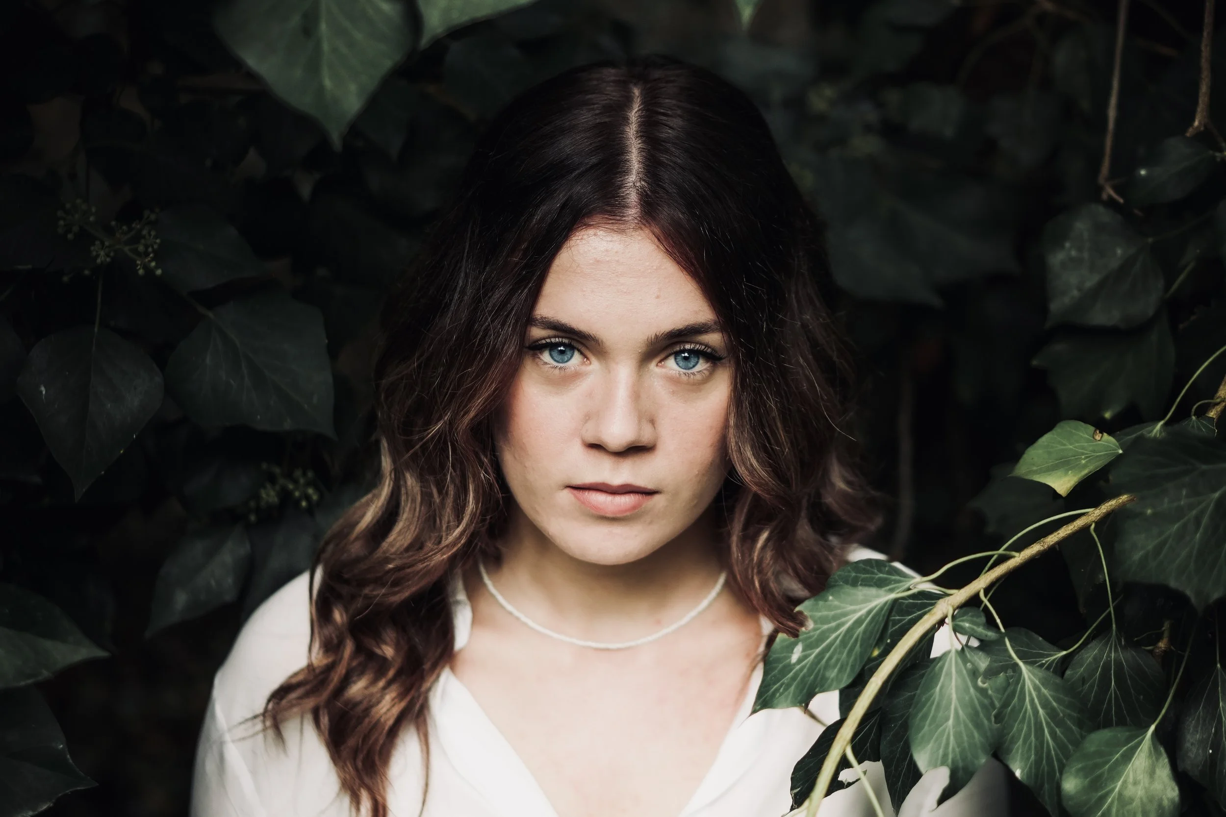 Ragazza con capelli castani e occhi azzurri tra foglie verdi