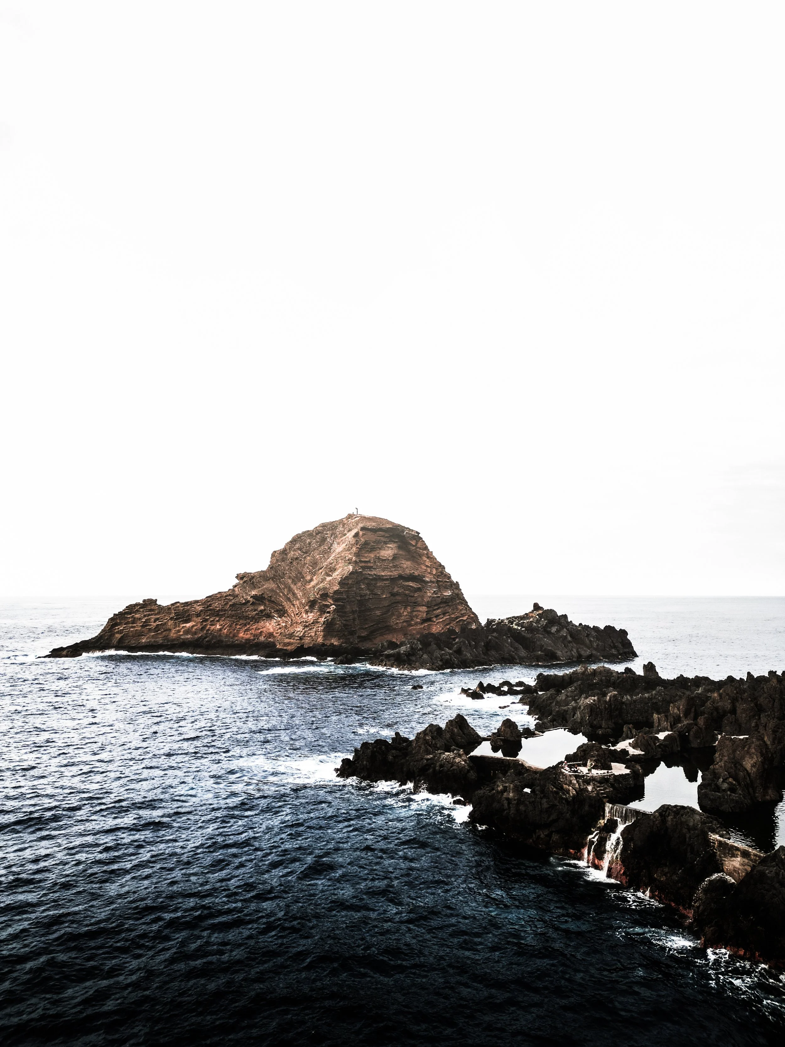 Isola rocciosa nel mare con onde che si infrangono contro le rocce, cielo molto chiaro
