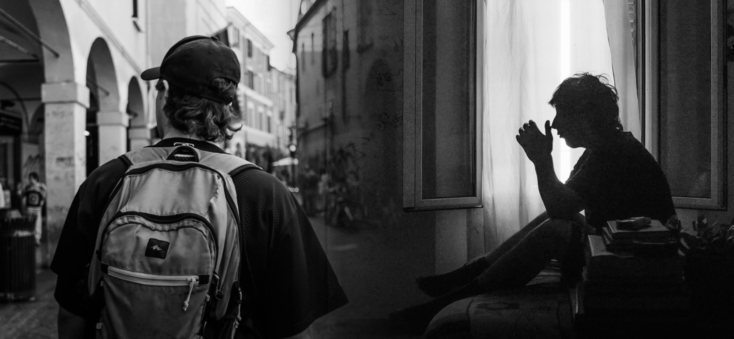 Un uomo con uno zaino osserva una donna seduta dietro una finestra, in un'ambientazione urbana. La scena è in bianco e nero.