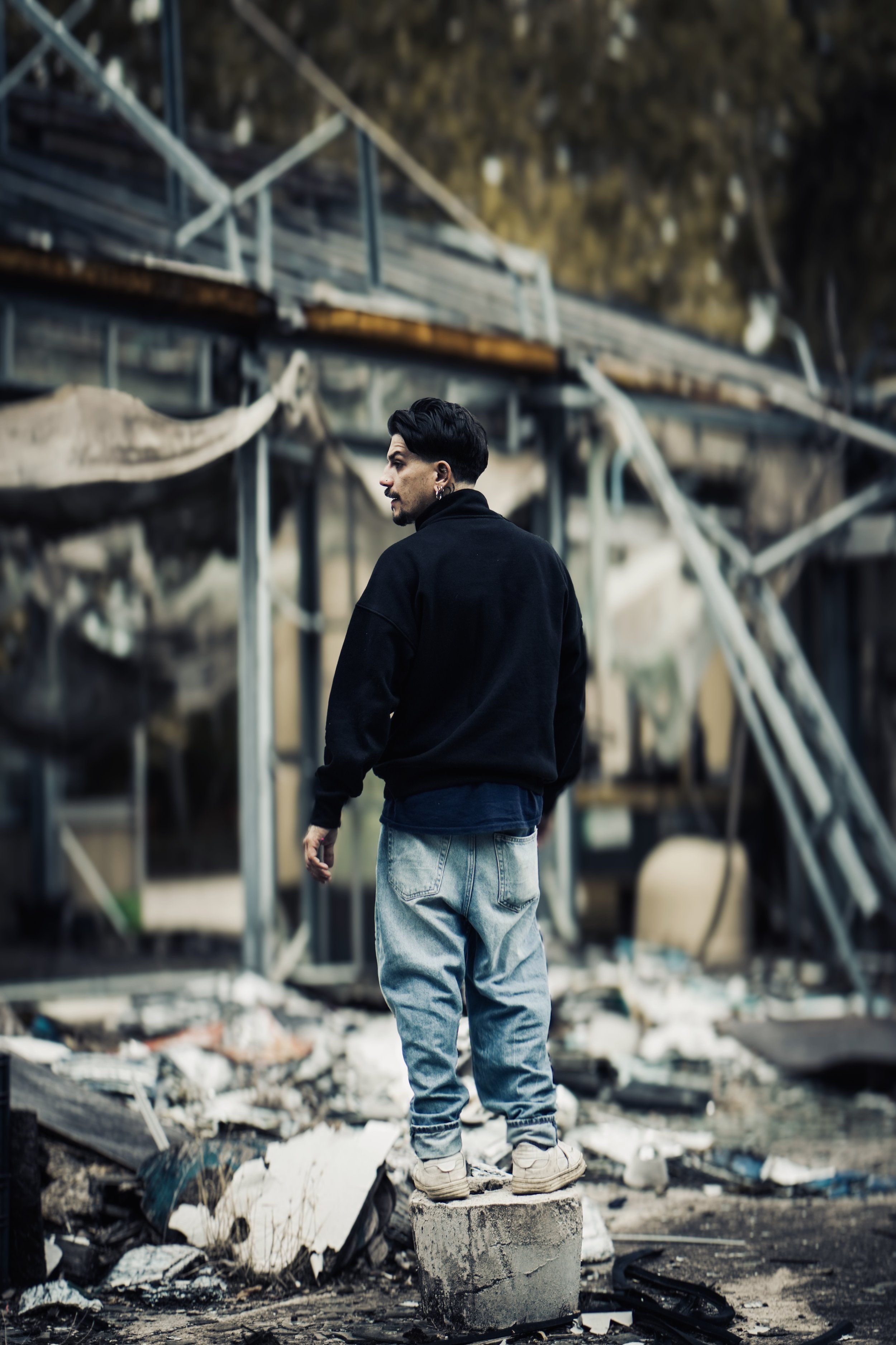 Persona che si trova su un blocco di cemento tra detriti e rovine di una costruzione danneggiata.