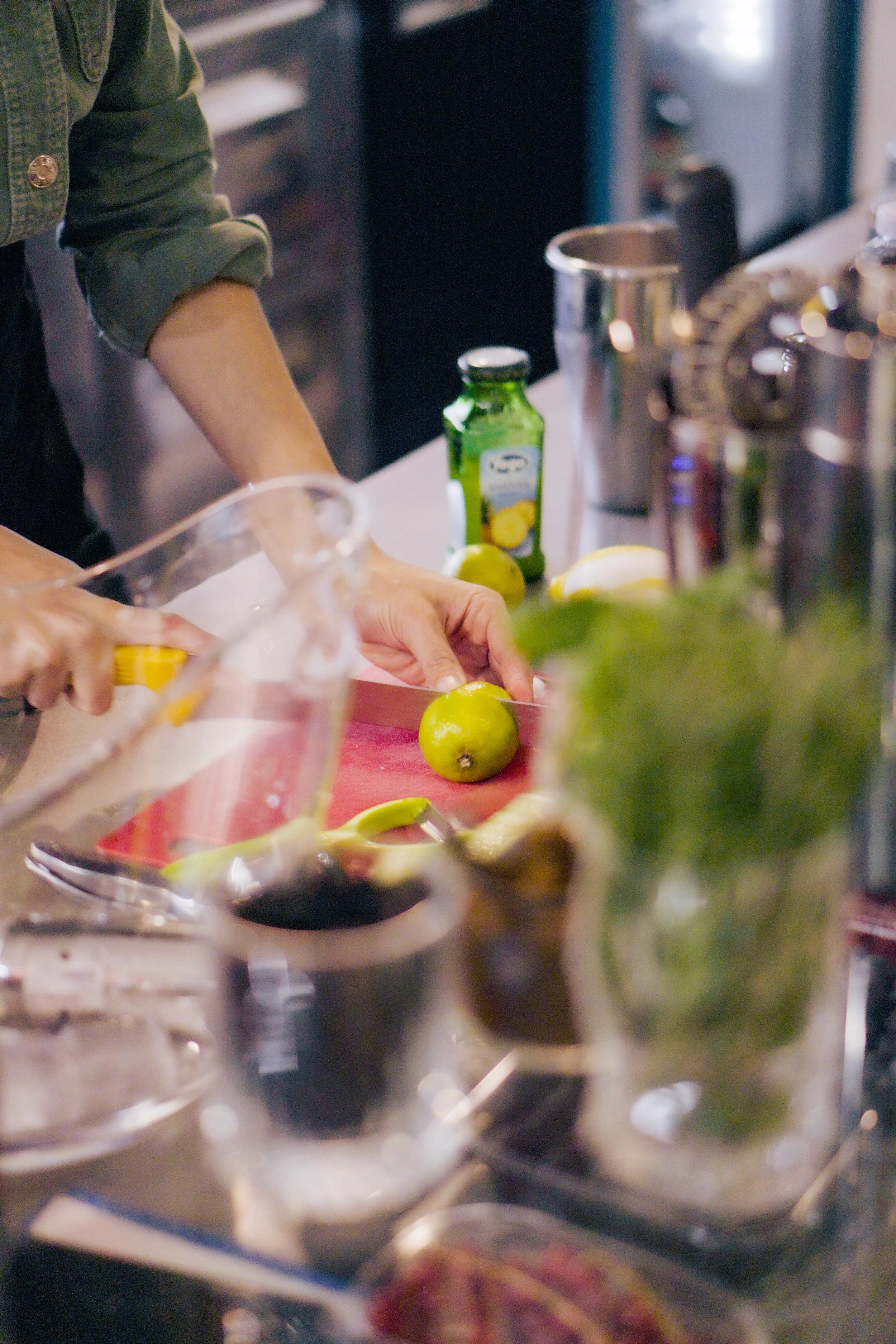 Persona che taglia un limone su un tagliere rosso in una cucina, con vari ingredienti e utensili intorno.