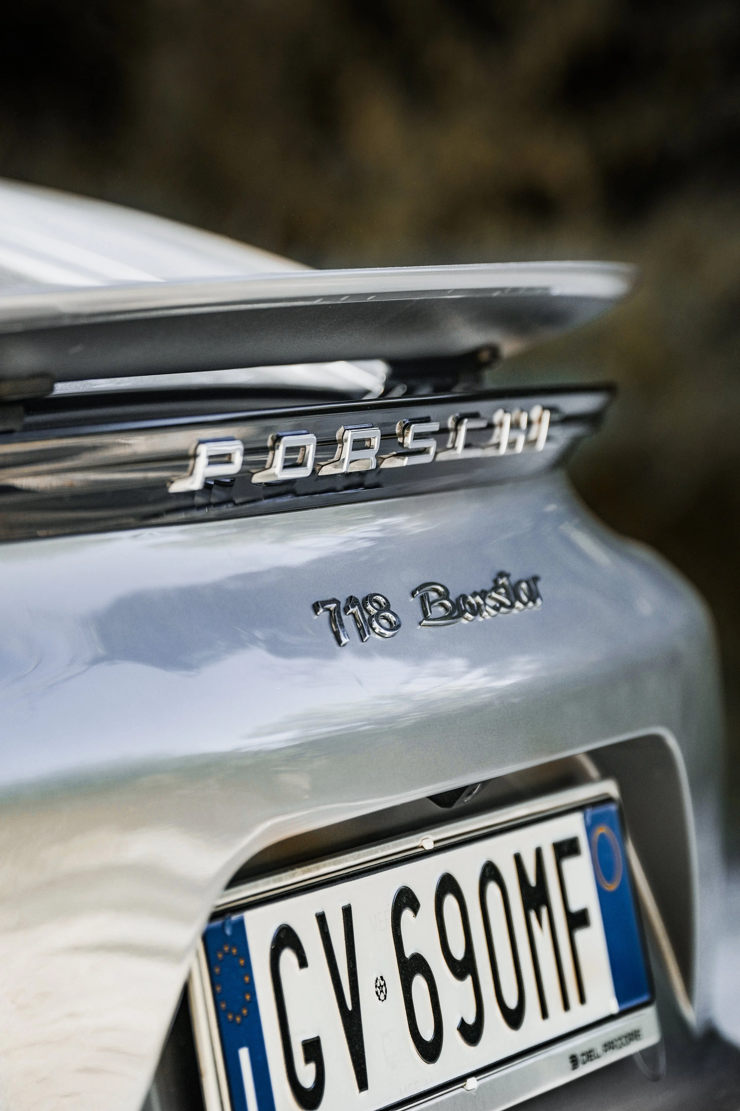 Particolare della parte posteriore di una vettura Porsche con badge '718 Boxster' e targa europea 'GV 69QME'.