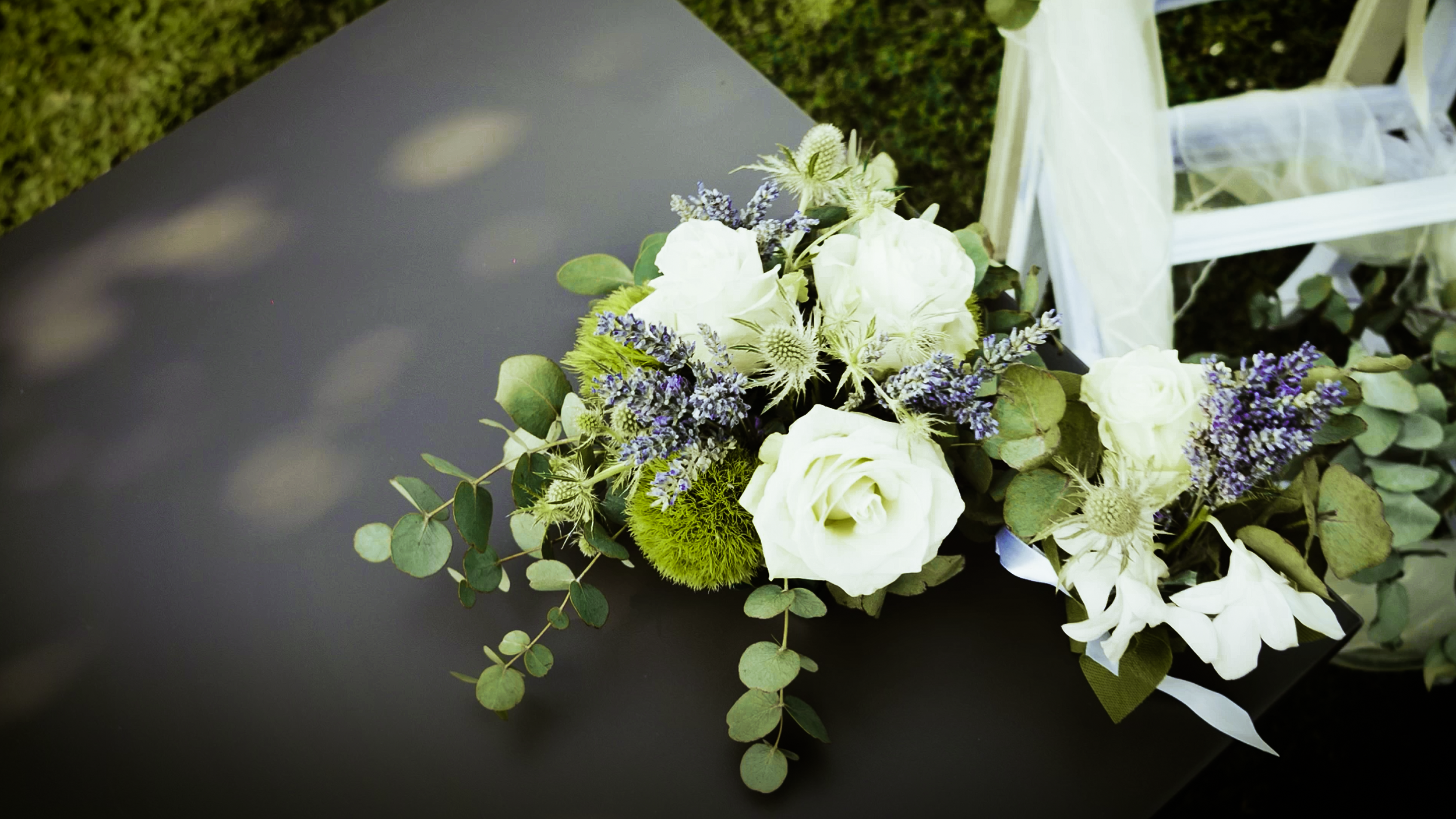Bouquet di fiori bianchi e lilla con foglie verdi, su una superficie scura, parte di un allestimento decorativo.