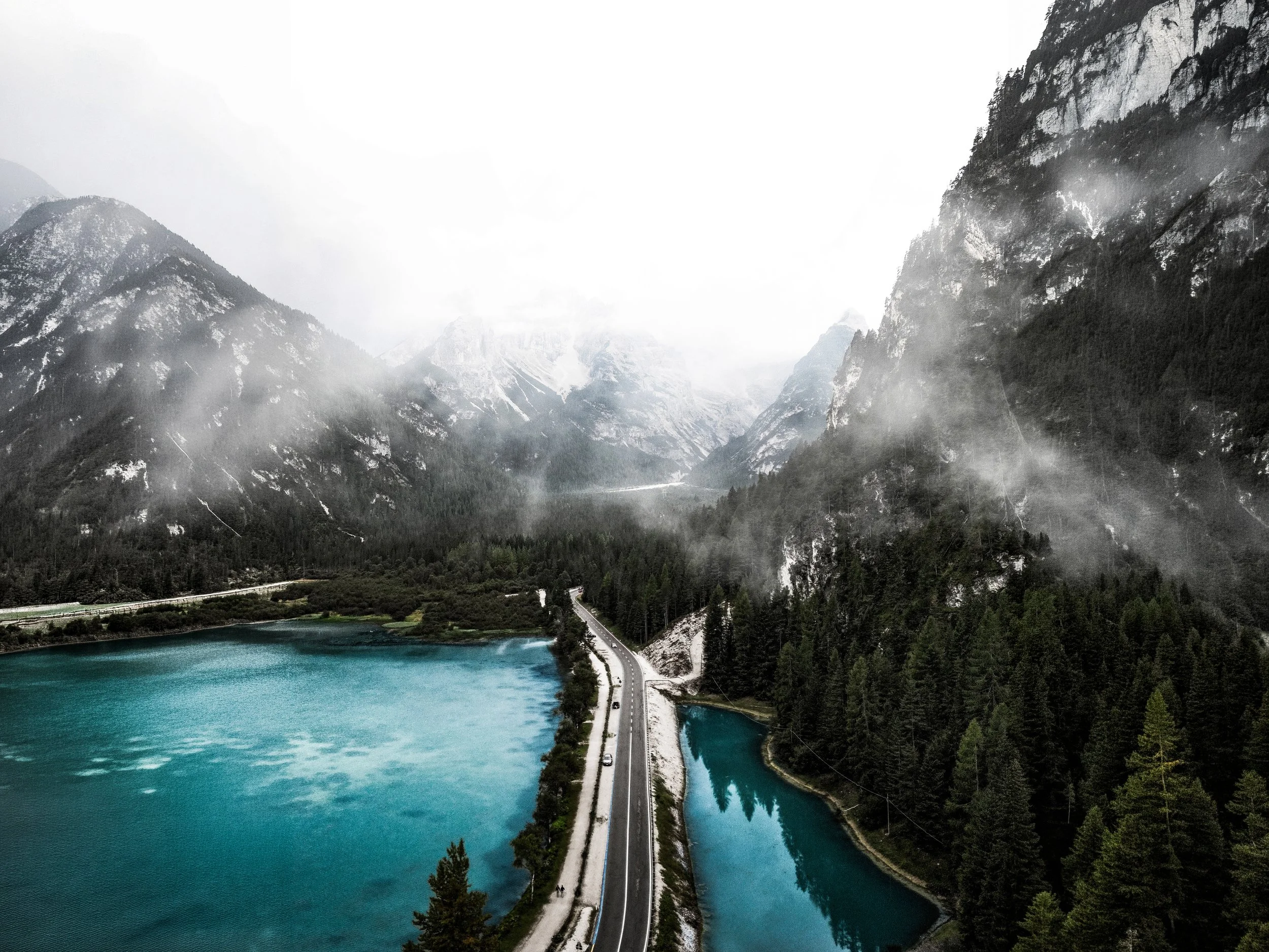 Paesaggio montano con laghi e foresta, strada tra le acque e le montagne avvolte da nebbia