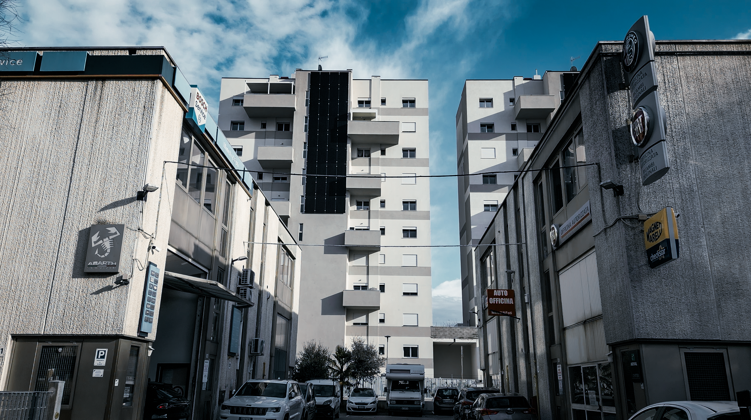 Città con palazzi moderni e automobili parcheggiate in strada, segni di negozi e uffici commerciali lungo la via.