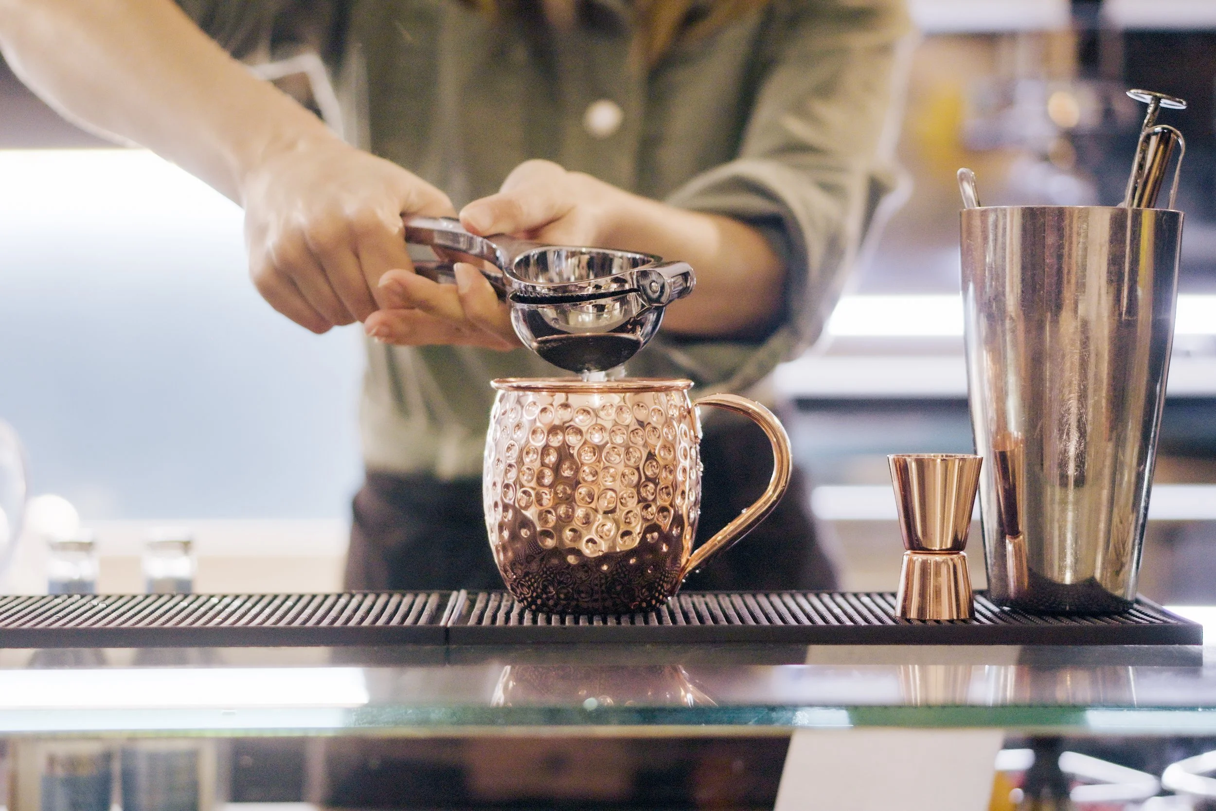 Un barista versa il caffè attraverso un colino in una tazza di metallo rosato con una superficie a pallini.