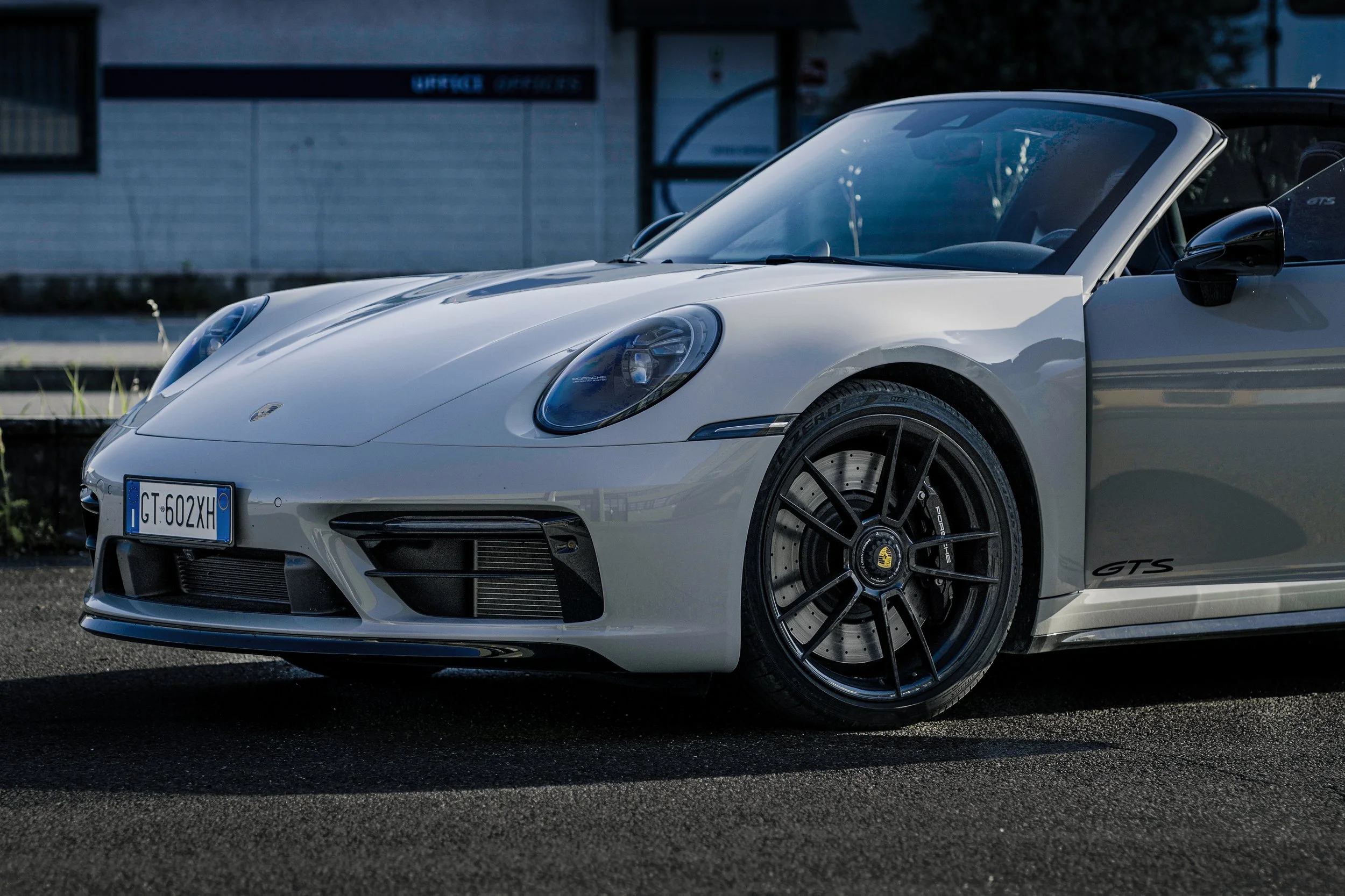 Auto sportiva Porsche 911 GTS Cabrio bianca con pneumatici neri e cerchi sportivi, parcheggiata su strada asfaltata.