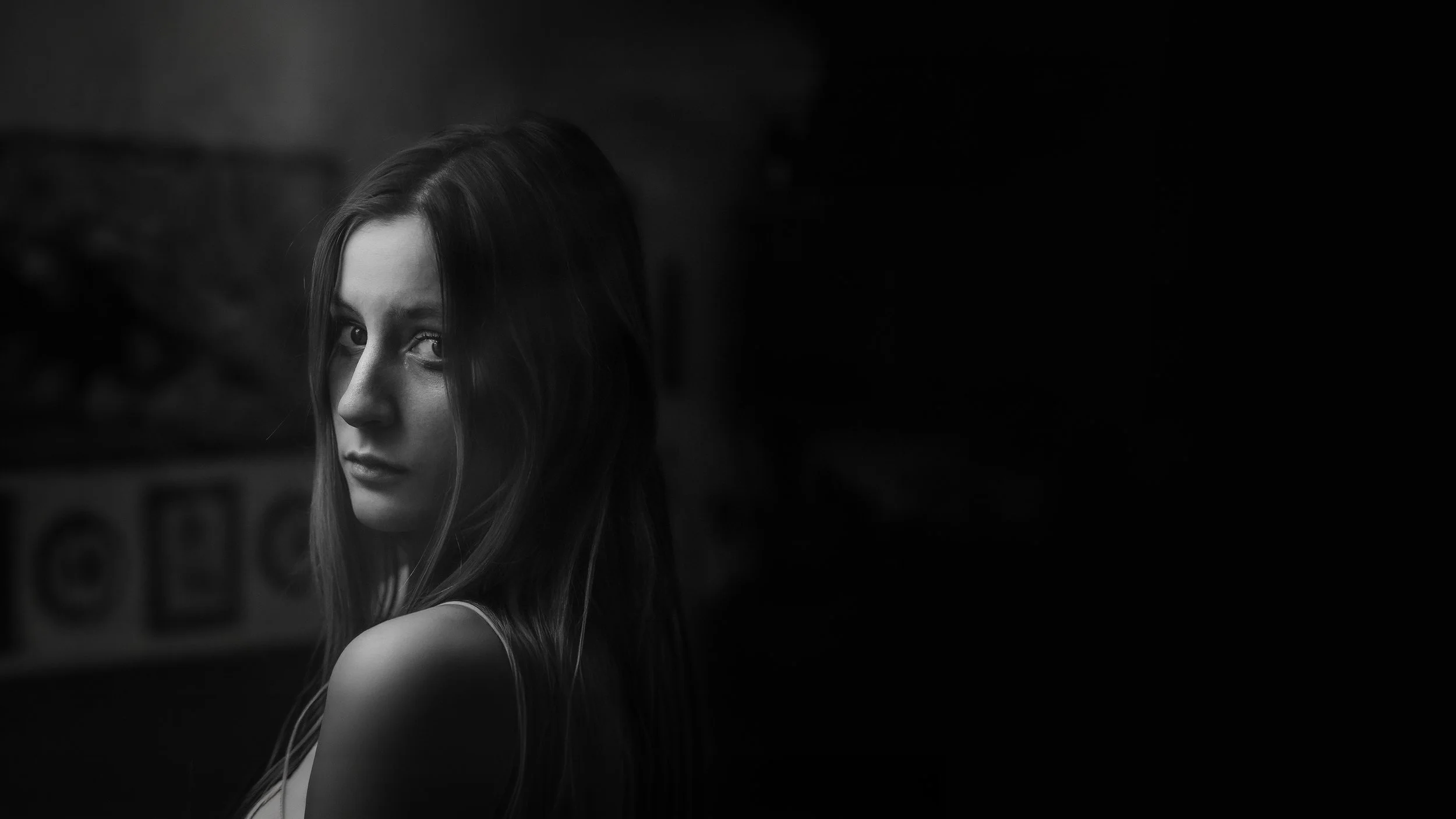 Ragazza con lunghi capelli castani che guarda in maniera intensa, ritratto in bianco e nero con sfondo scuro