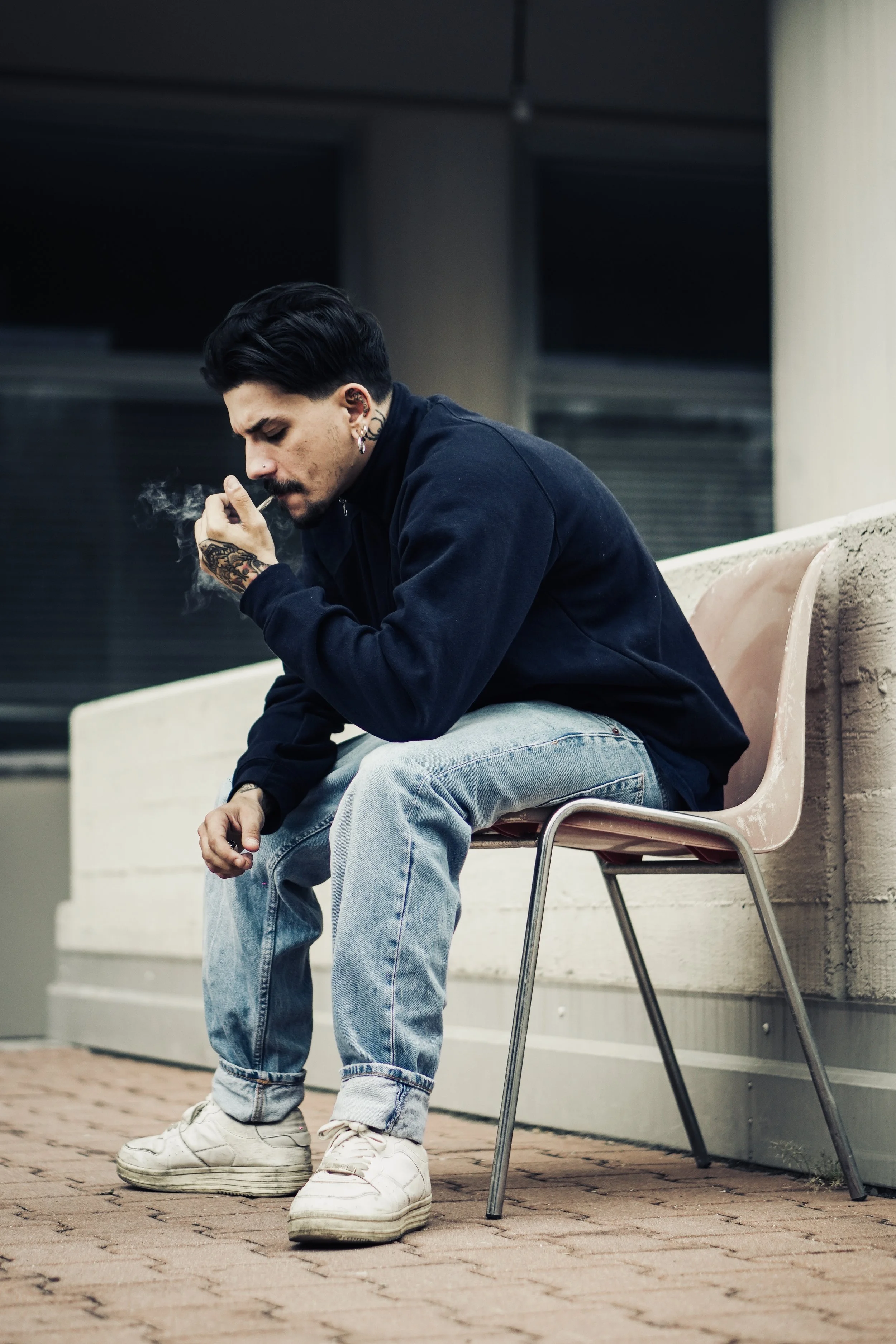 Uomo seduto su una sedia che fuma una sigaretta in un'area urbana.