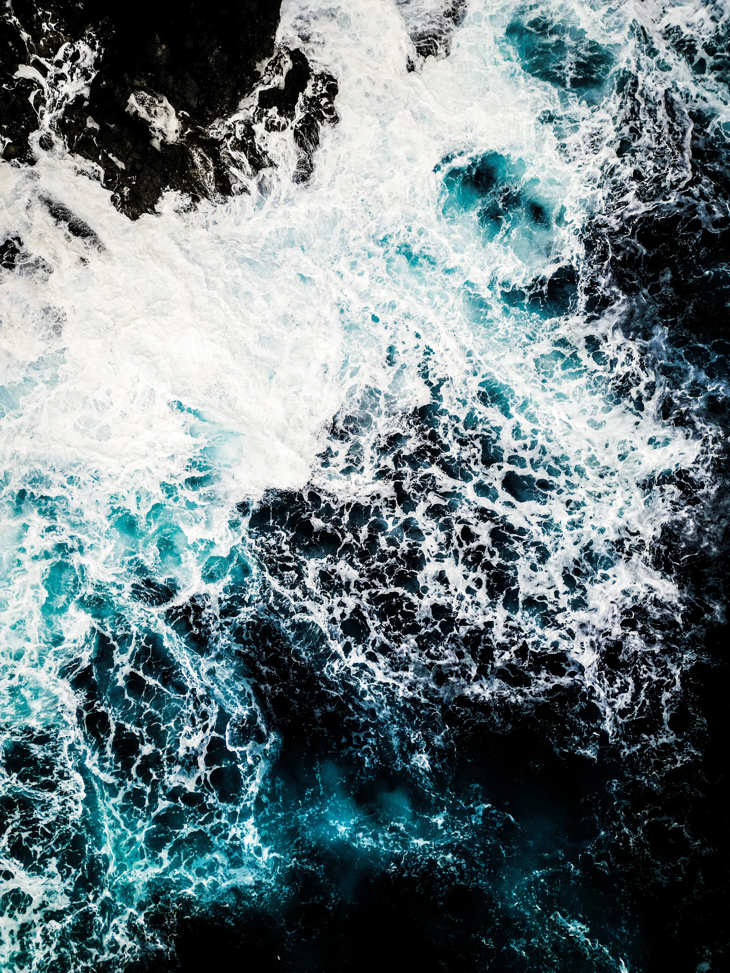 Onde di mare che si infrangono contro le rocce con schiuma bianca e acqua blu scura.