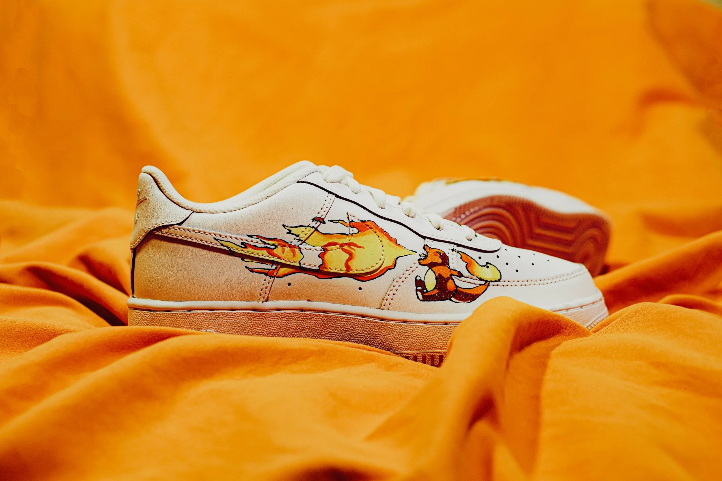 Scarpa da ginnastica bianca con disegno di un drago di fuoco e un altro animale, su sfondo arancione.