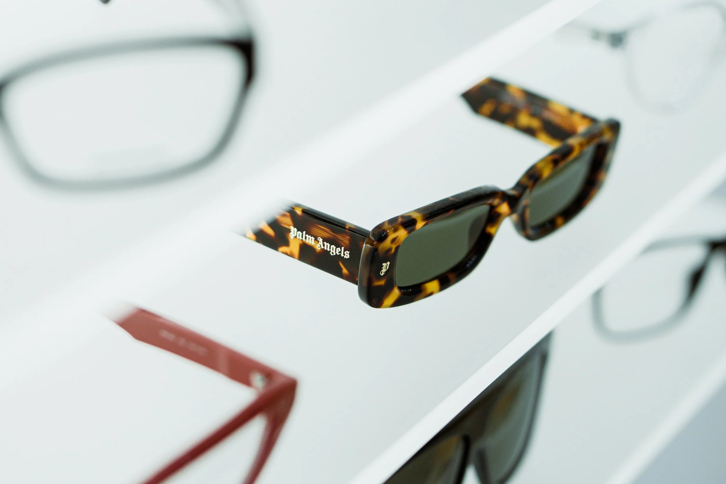 Occhiali da sole con montatura tartarugata e l'interno scritto 'palm angels' su una mensola bianca