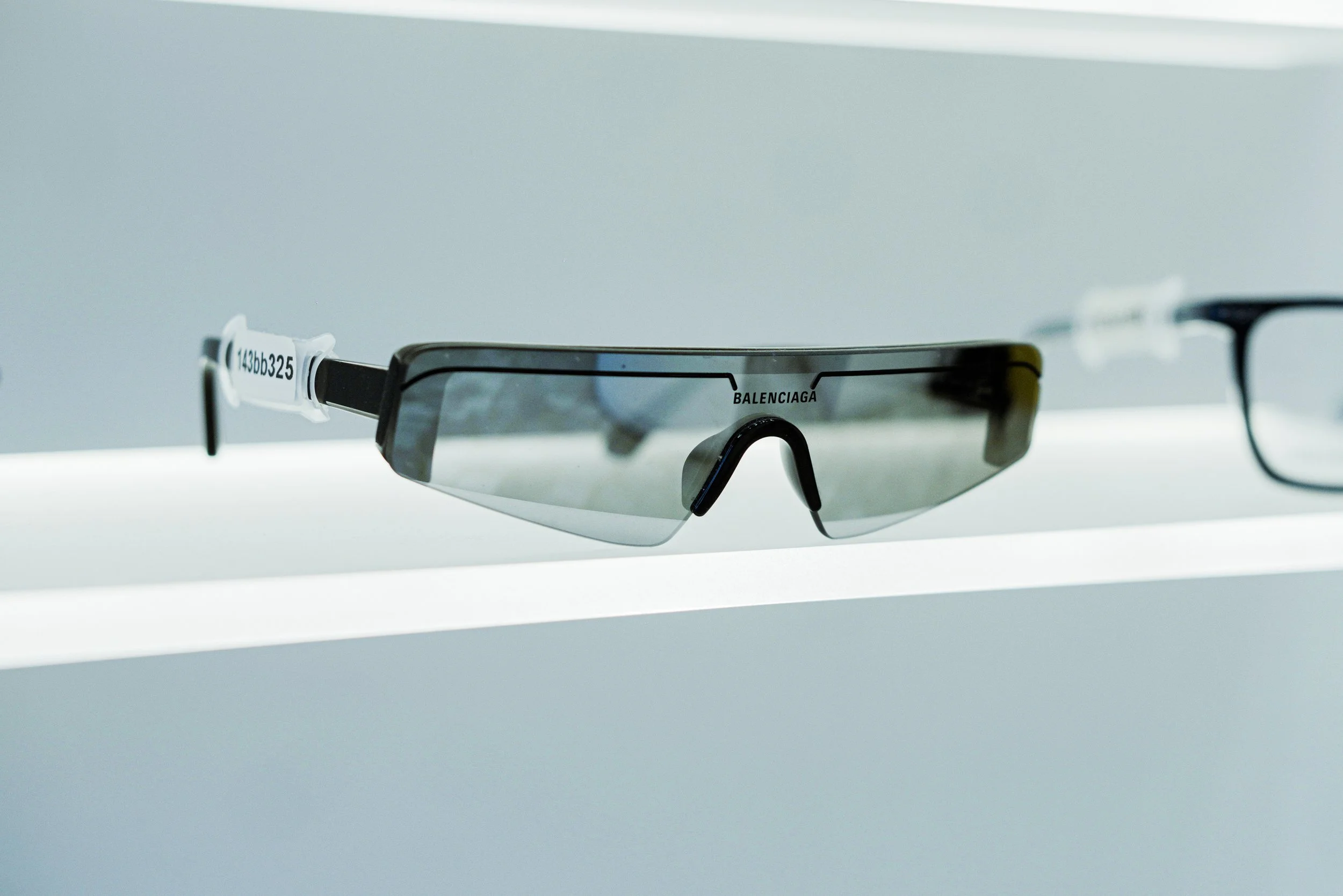 Occhiali da sole sportivi di marca Balenciaga con lenti riflettenti, posizionati su una superficie bianca.