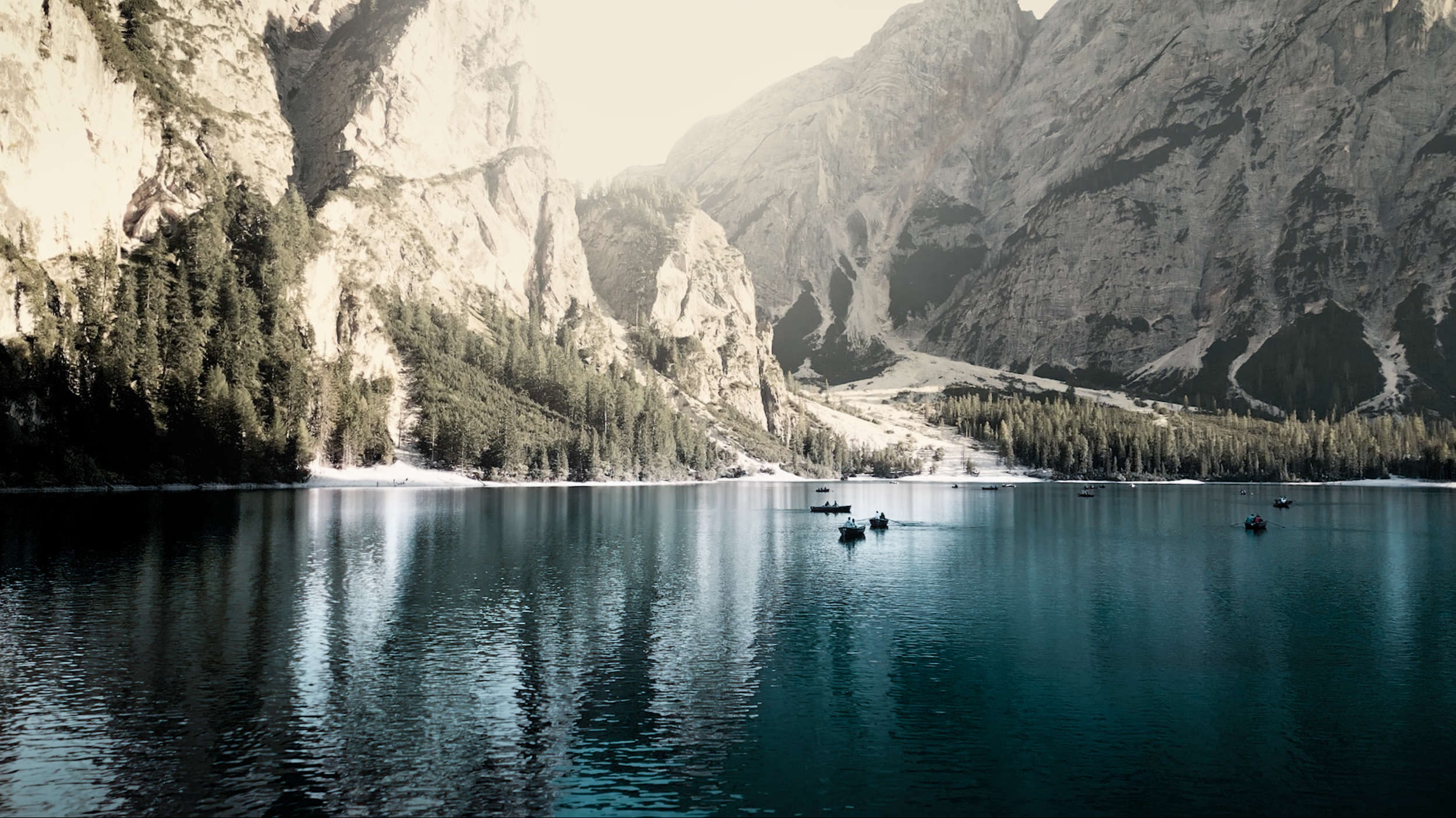 Lago con barche, circondato da montagne e foresta in Italia