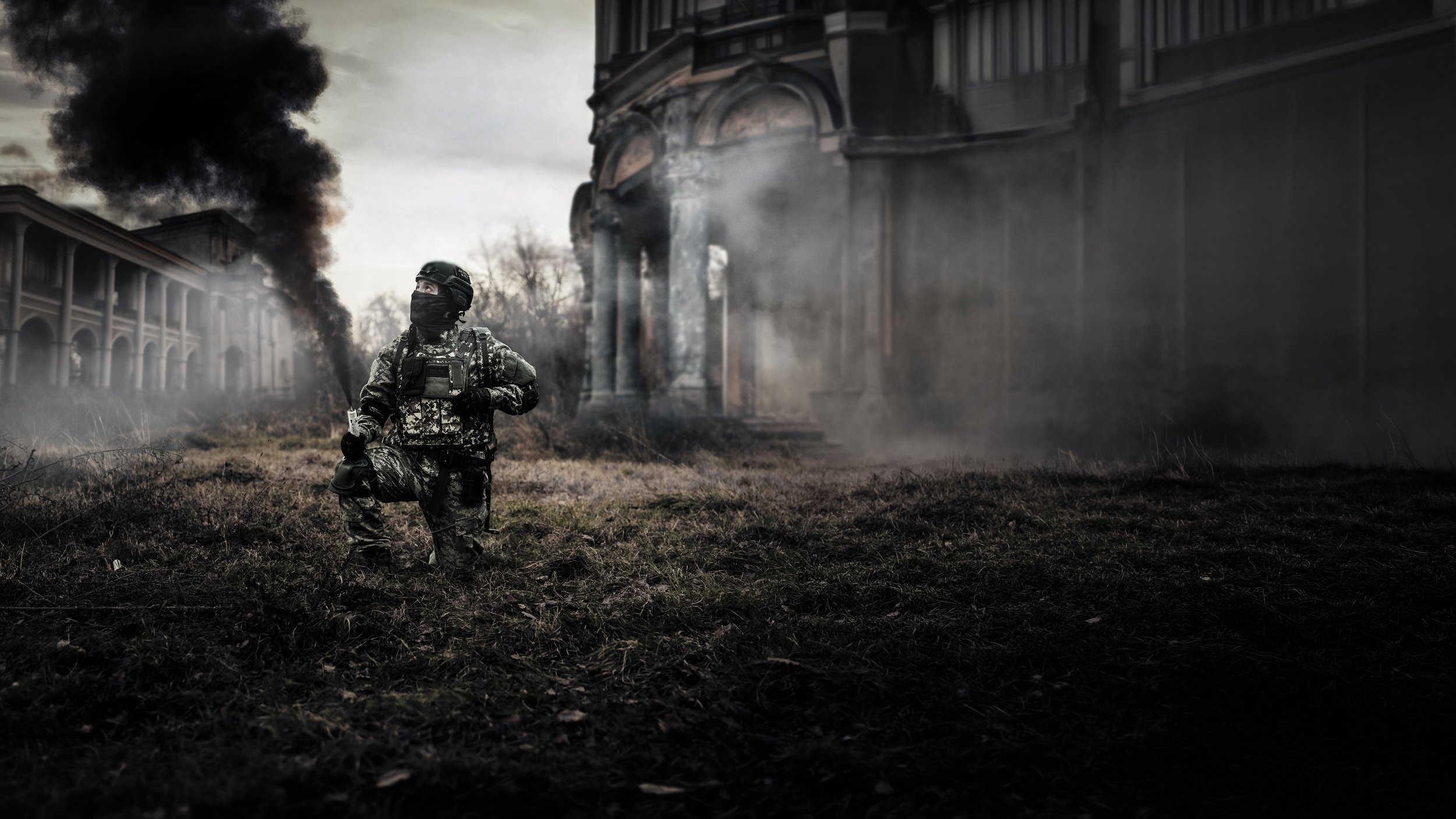 Soldato in abbigliamento mimetico con mascherina, in ginocchio su un terreno bruciato, con fumo nero che esce da un edificio in rovina sullo sfondo, atmosfera grigia e cupa.