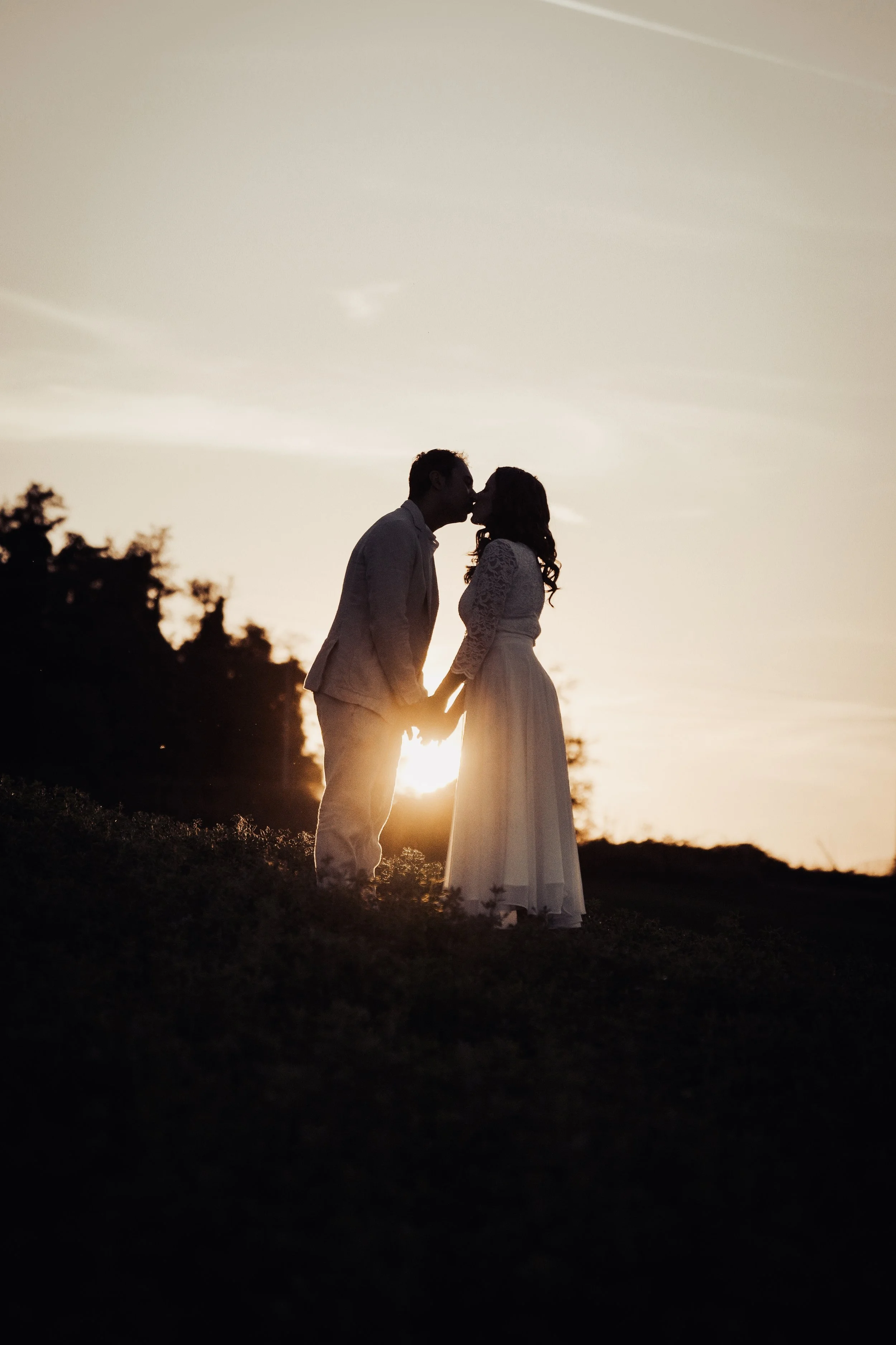 Silhouette di una coppia di persone in abiti eleganti che si baciano al tramonto.