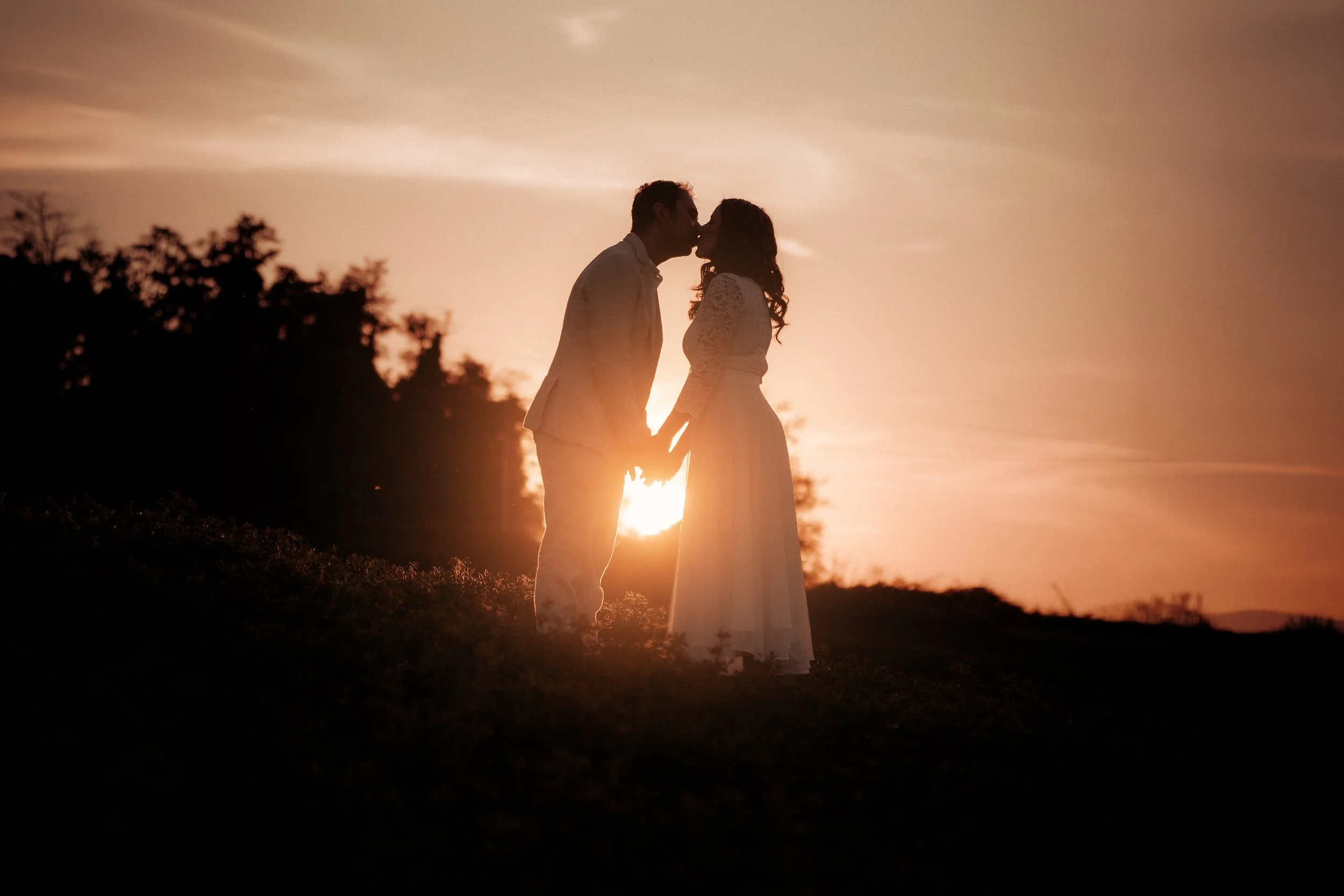Una coppia innamorata si bacia durante il tramonto, silhouette contro un cielo arancione