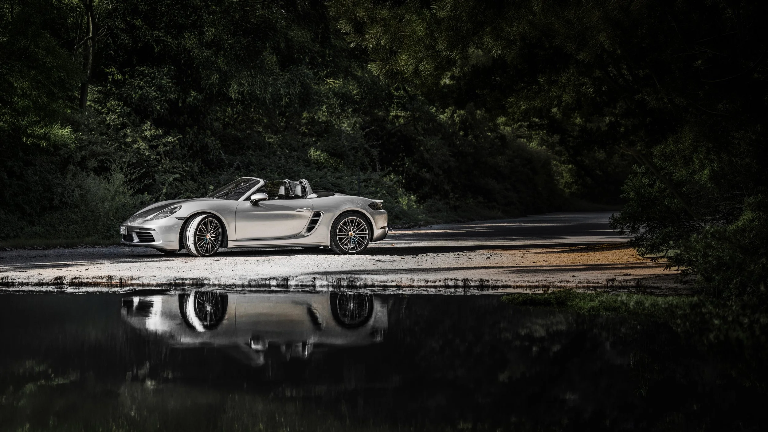 Auto sportiva convertibile argento parcheggiata vicino a un laghetto in una foresta