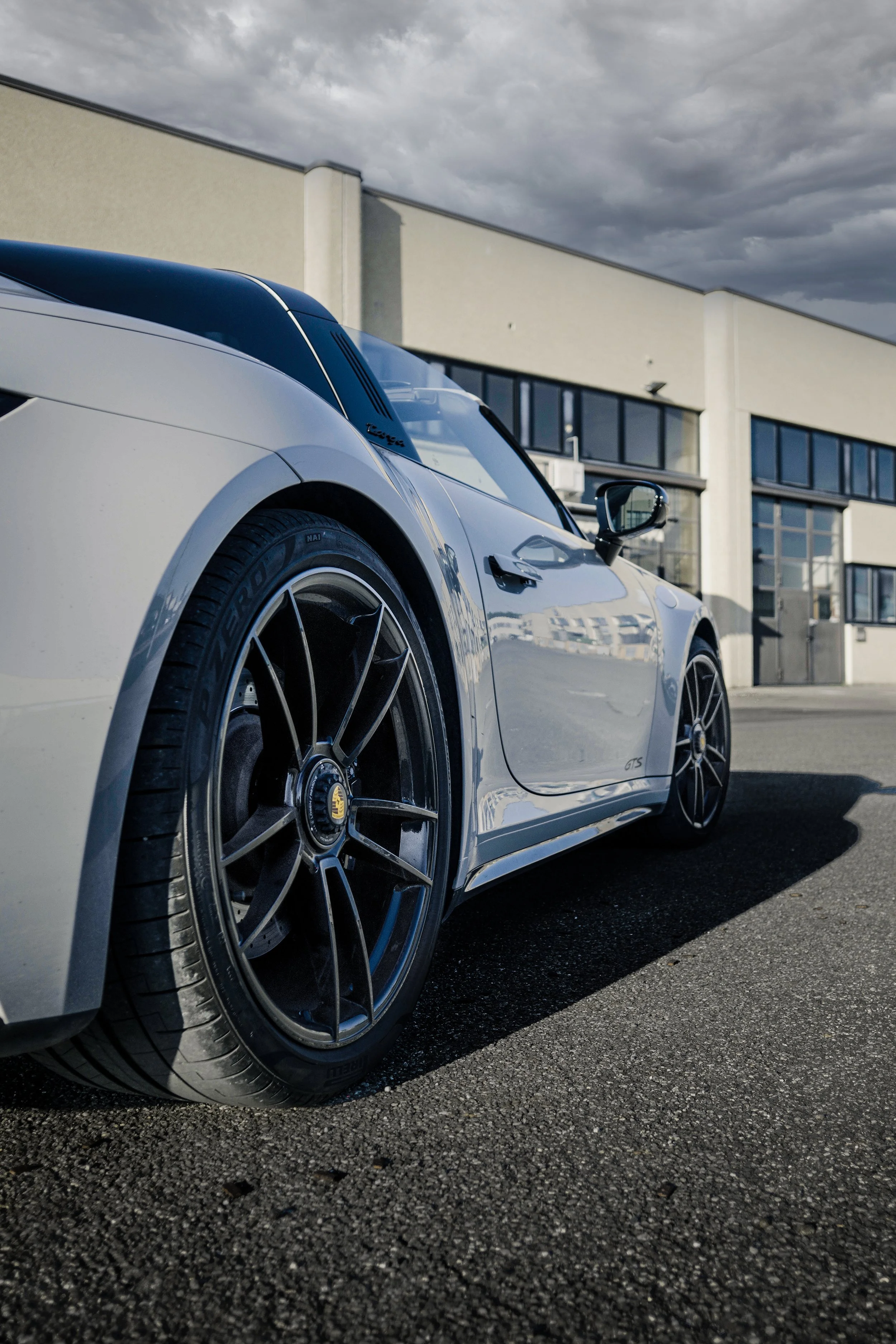 Auto sportiva bianca con pneumatici a basse taree, parcheggiata su un parcheggio vuoto davanti a un edificio moderno, sotto un cielo nuvoloso.