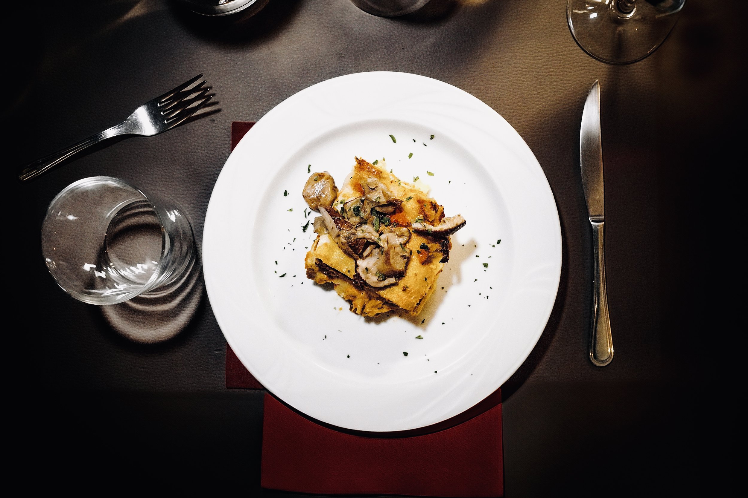 Piatti di lasagne con funghi, servito su un piatto bianco, con bicchiere d'acqua e posate in un tavolo apparecchiato