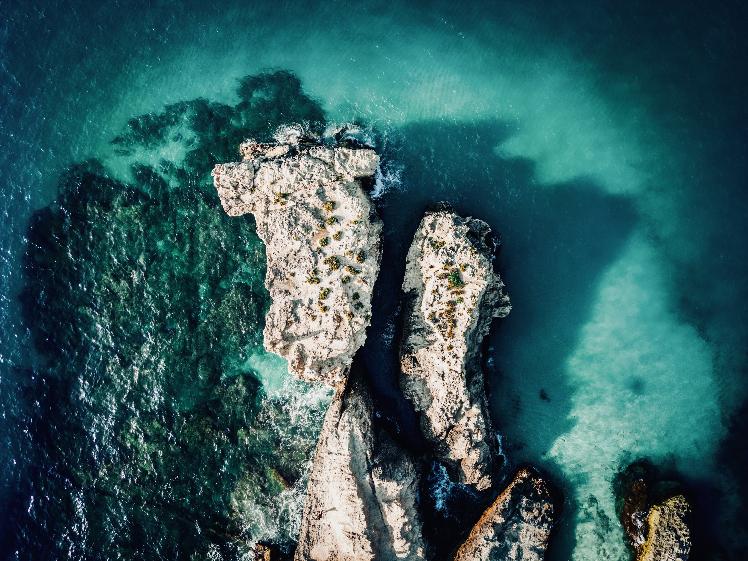 Scorcio di rocce in mare fotografate dall'alto con acque azzurre e verde professionali.