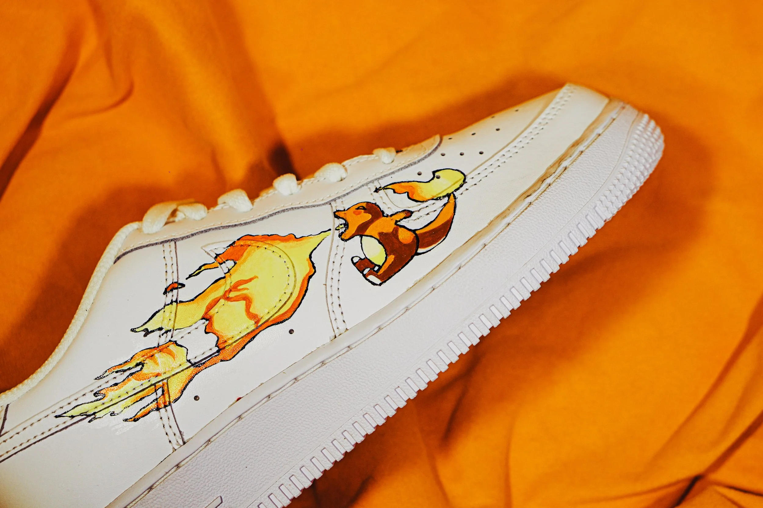 Sneaker bianco con disegni artistici di draghi colorati, posato su tessuto arancione.