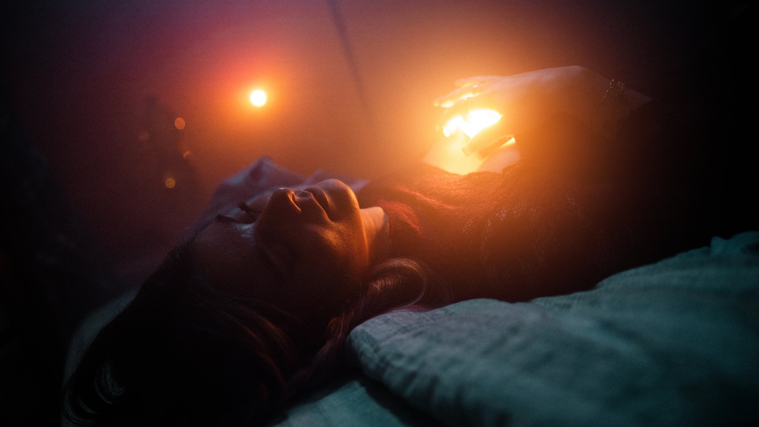 Una persona sdraiata con gli occhi chiusi, illuminata da luci calde e una luna nel cielo notturno.